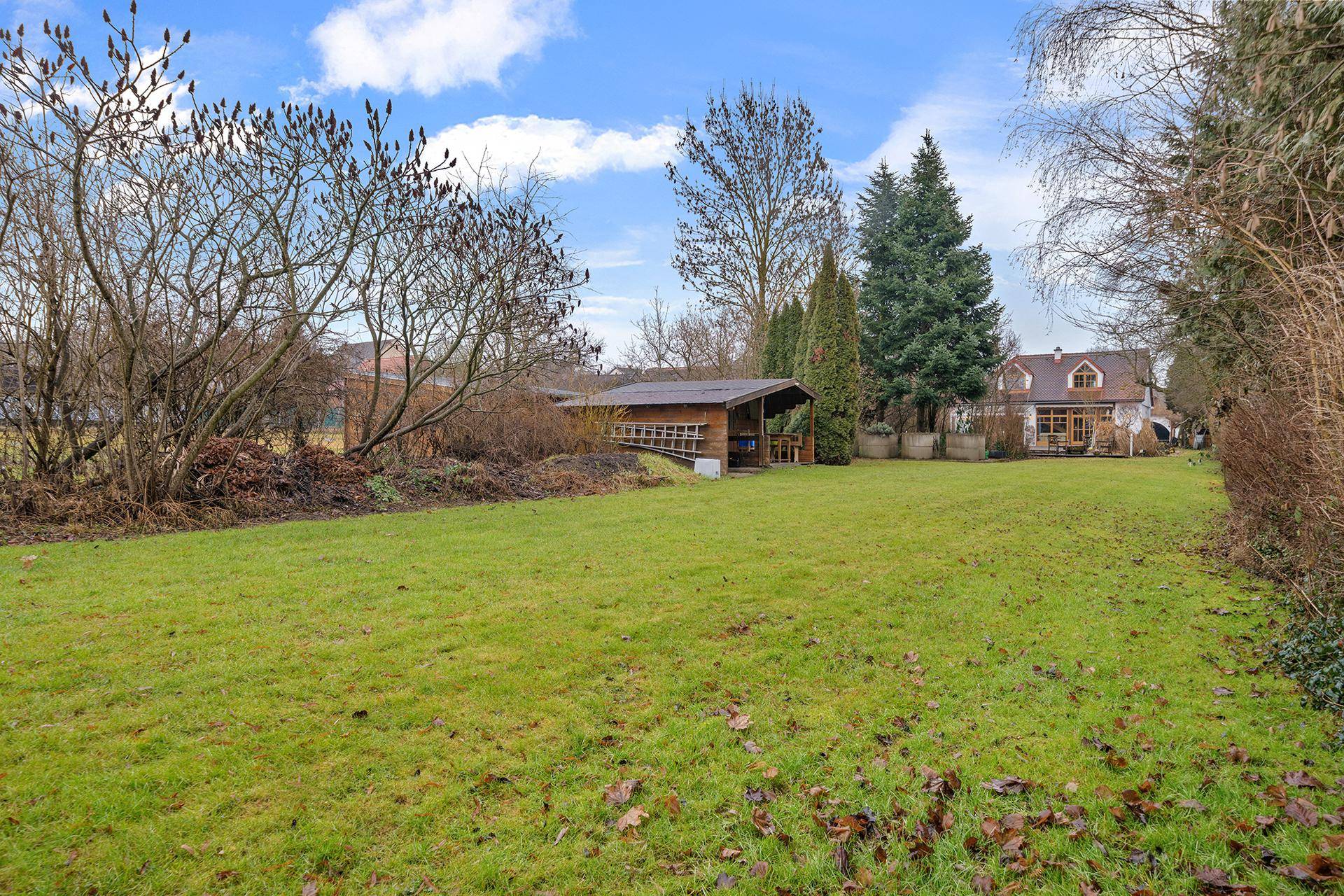 Weitläufiger grüner Garten mit Rasenfläche, Bäumen und einem kleinen Gartenhaus im Hintergrund.