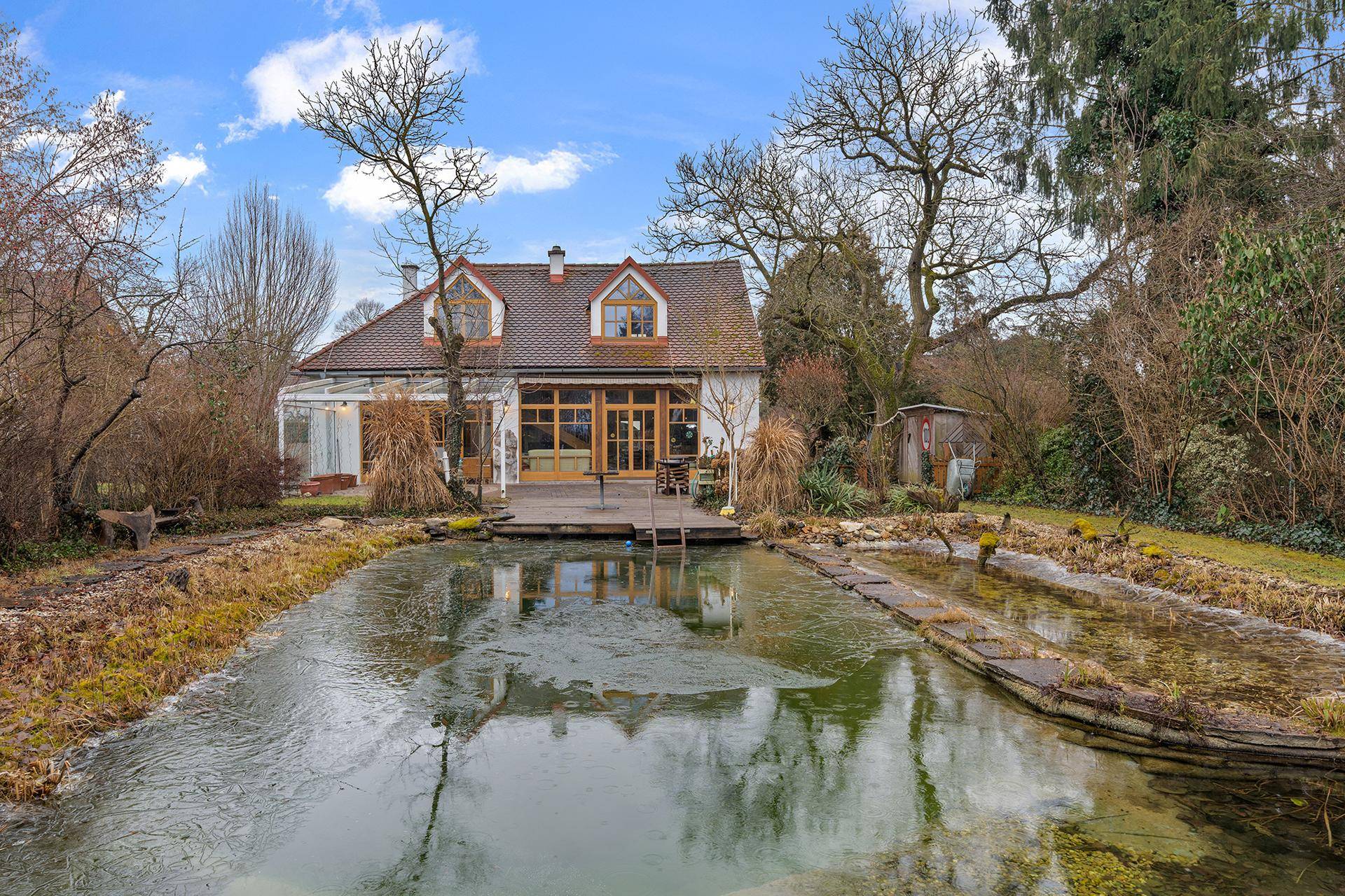 Rückansicht des Hauses mit großem Garten, natürlichem Teich und umgebender Vegetation im Winter.