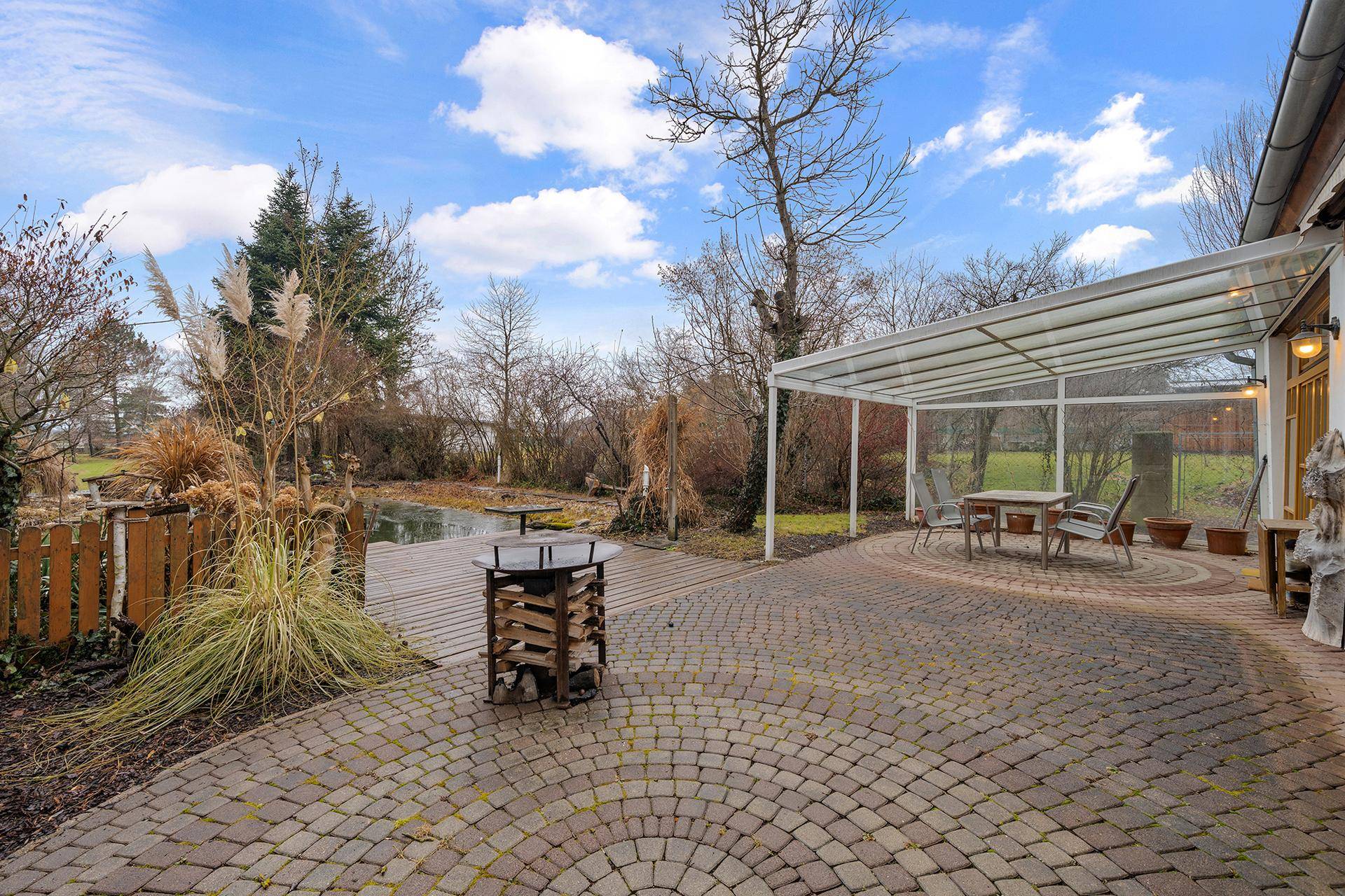 Große gepflasterte Terrasse mit überdachtem Sitzbereich und Blick auf den Gartenteich.