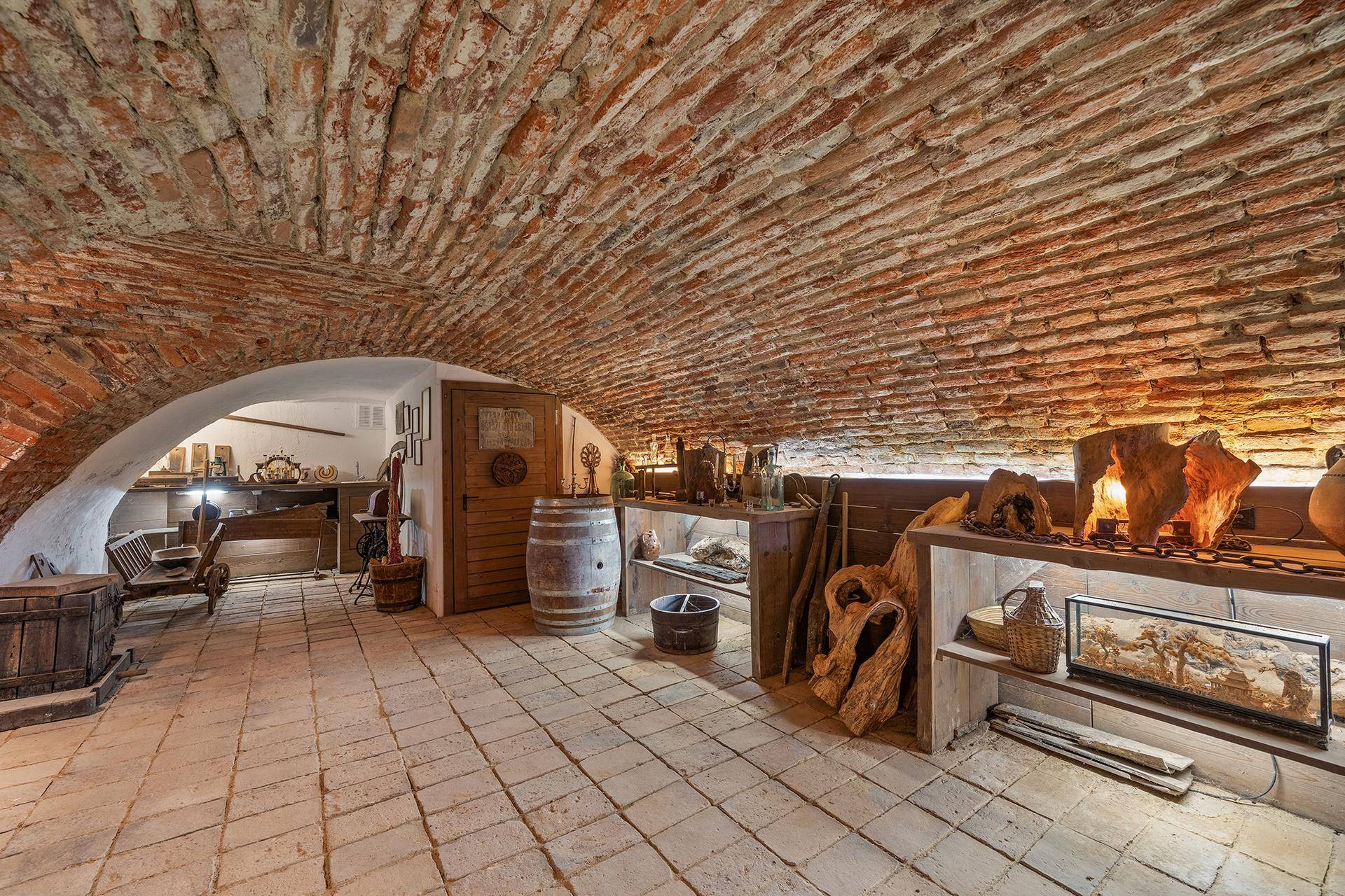 Historischer Gewölbekeller mit Ziegeldecken, Fliesenboden und rustikaler Dekoration, ideal für Weinlagerung.
