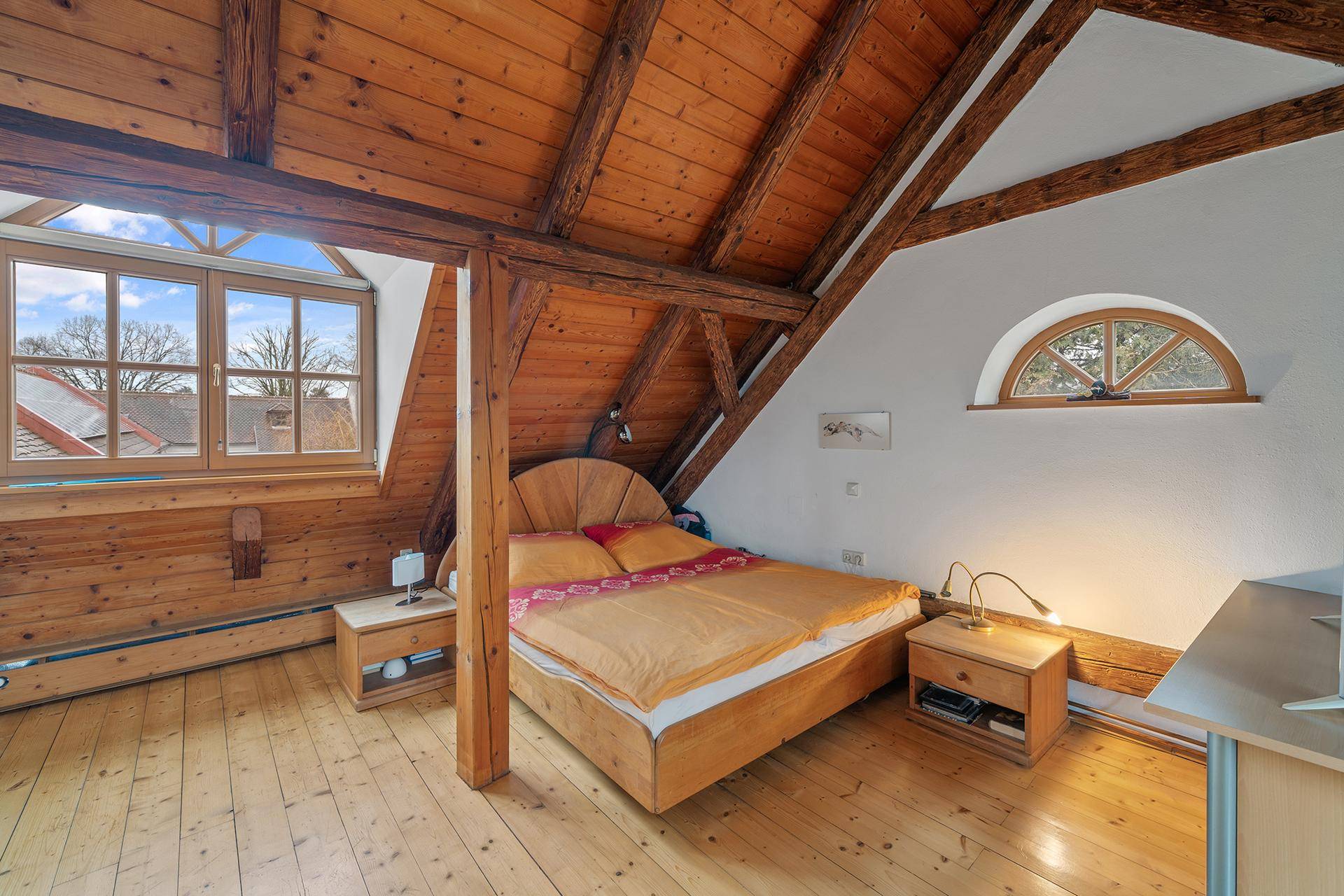 Schlafzimmer im Dachgeschoss mit Holzbalken, Dachschräge und großen Fenstern für viel Tageslicht.