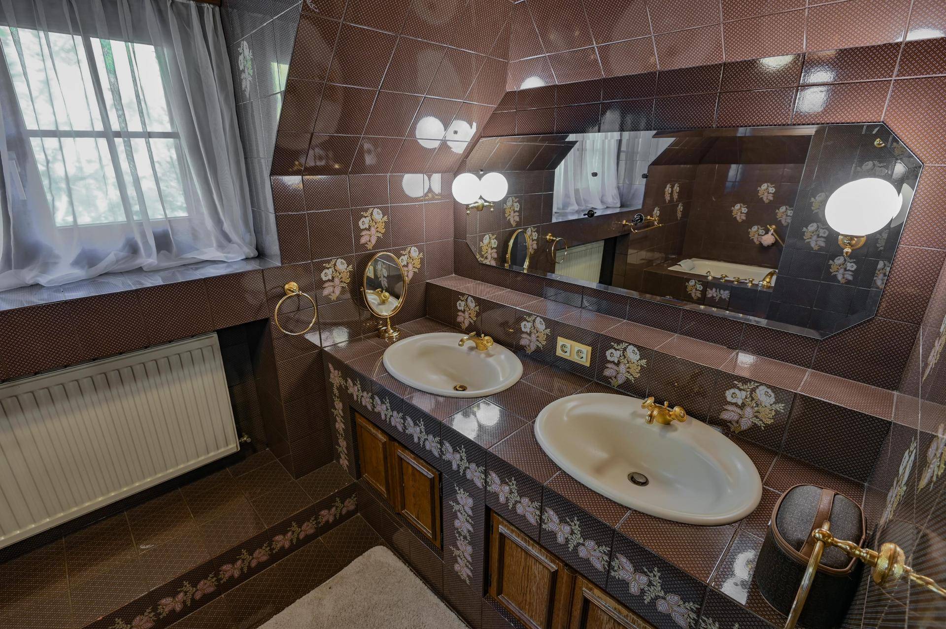 Badezimmer im 80er-Jahre-Stil mit braunen Fliesen, Doppelwaschbecken und großem Spiegel.