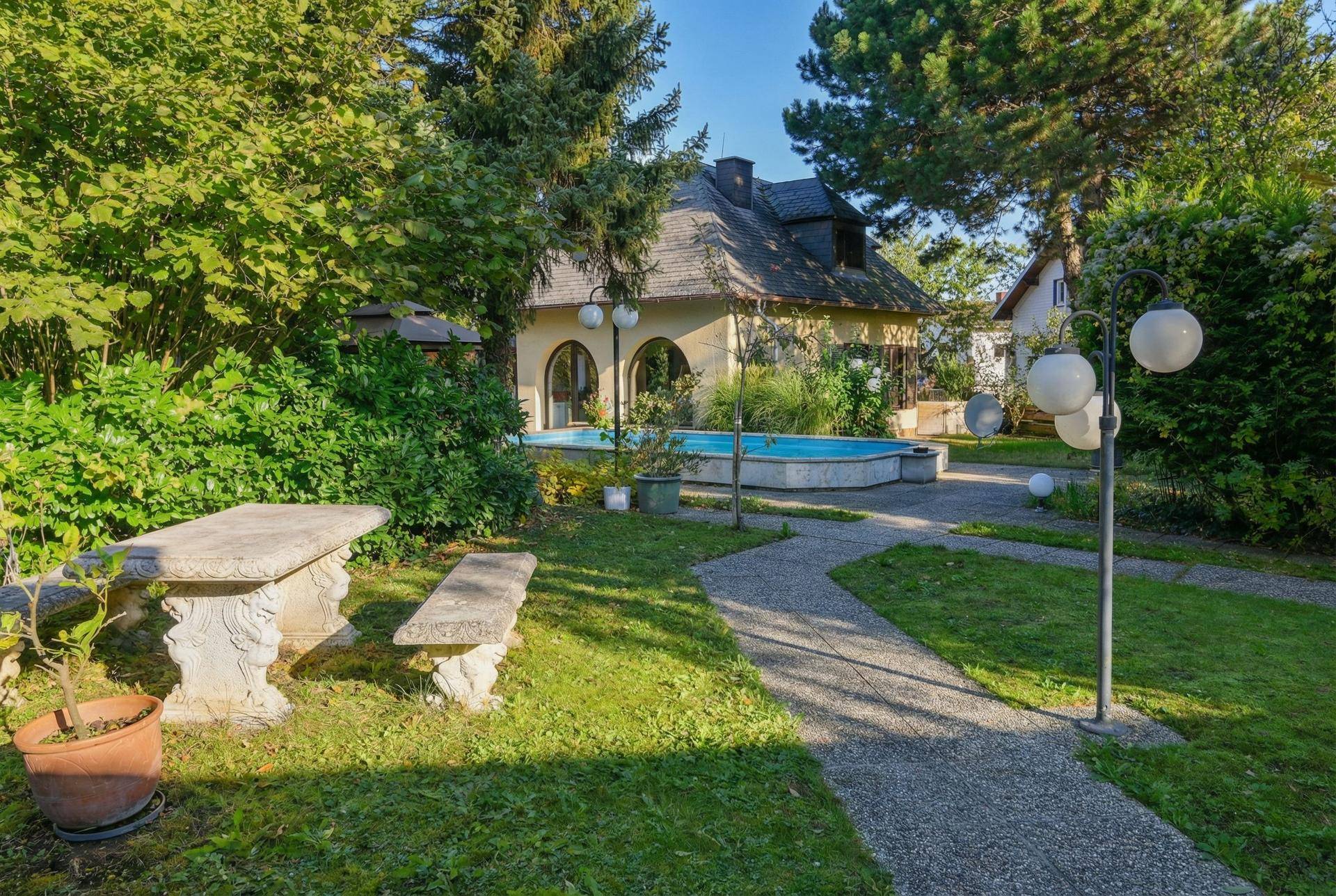 Idyllischer Gartenbereich mit Pool, alter Steinbank und üppiger Vegetation, perfekt zum Entspannen.