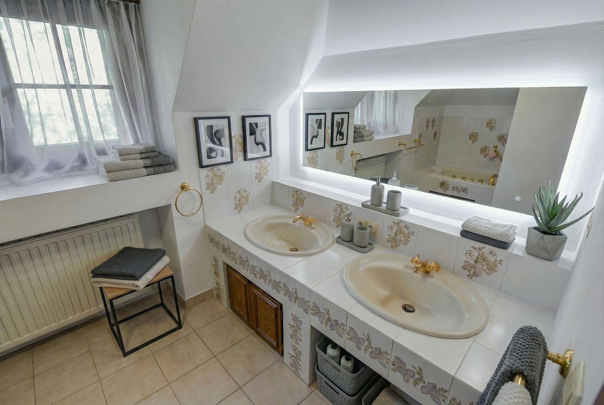 Modernisiertes Badezimmer mit weißen Fliesen, Doppelwaschbecken und beleuchtetem Spiegel.