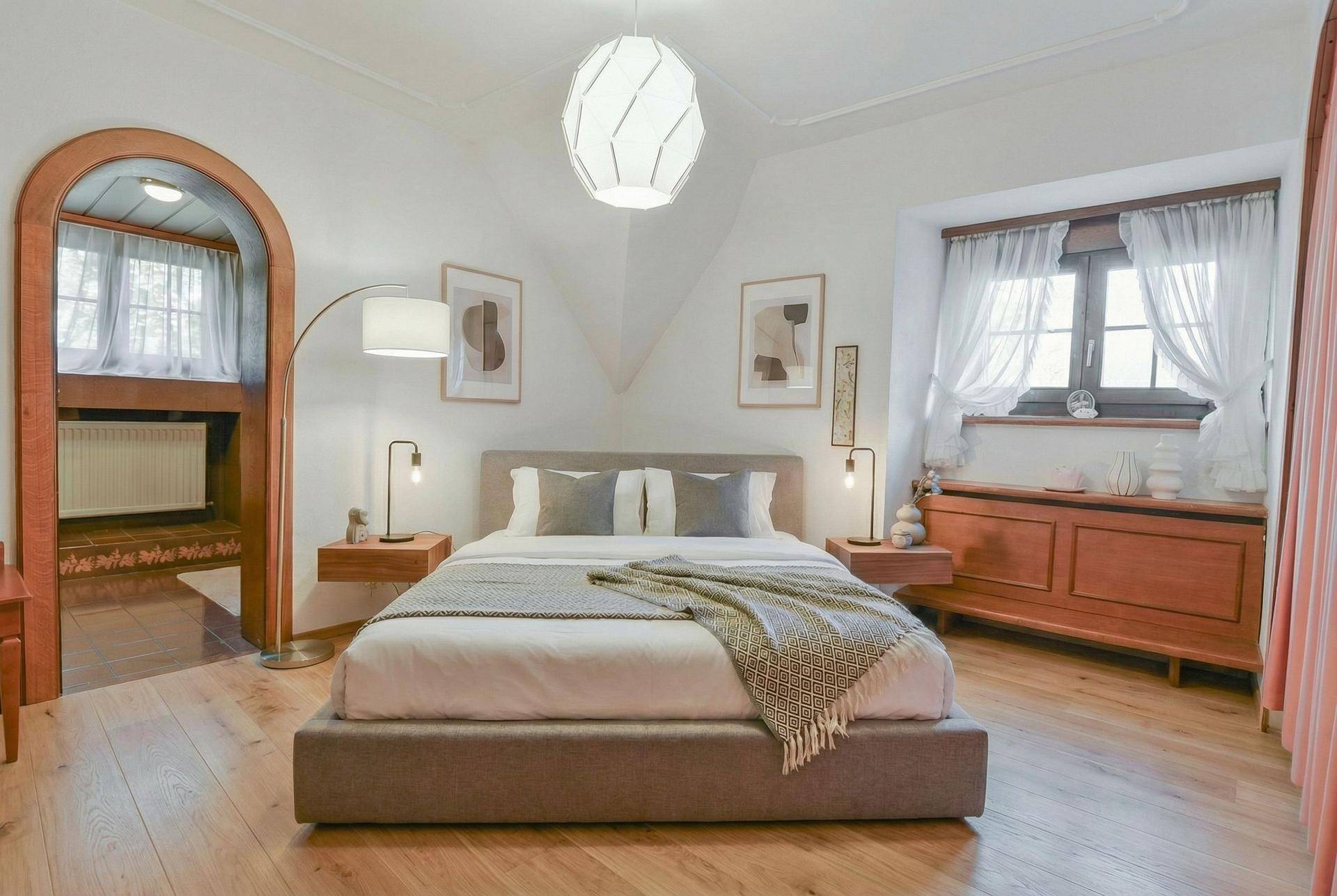 Modernisiertes Schlafzimmer mit schlichter Einrichtung, Holzboden und einem Bogenzugang zu einem Nebenraum.