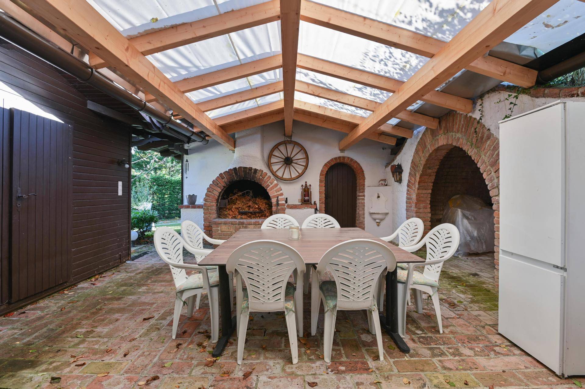Überdachter Essbereich im Freien mit großem Tisch, Backofen und Kühlschrank, ideal für Feste.