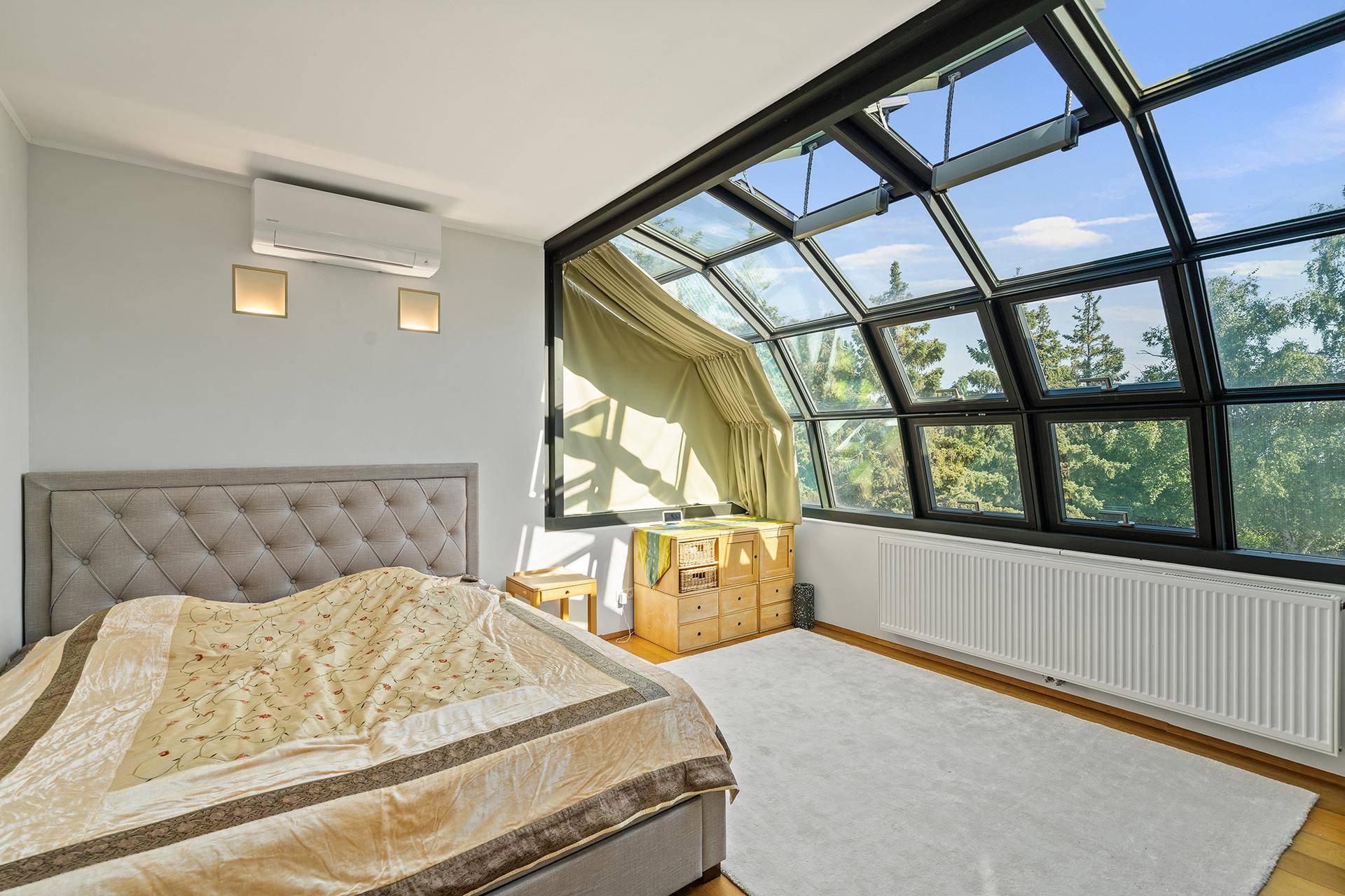 Schlafzimmer mit Klimaanlage und beeindruckender Glasfront, die viel Tageslicht hereinlässt.