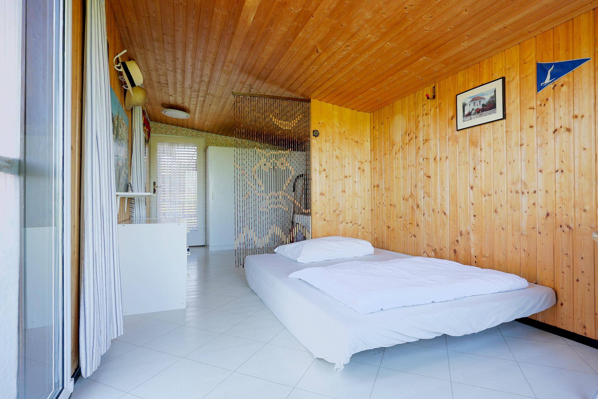 Helles Schlafzimmer mit Holzvertäfelung, weißem Fliesenboden und einem Einzelbett.