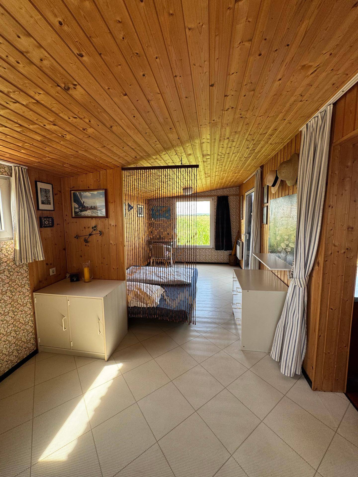Gemütliches Schlafzimmer mit Holzvertäfelung an Decke und Wänden sowie hellem Fliesenboden.