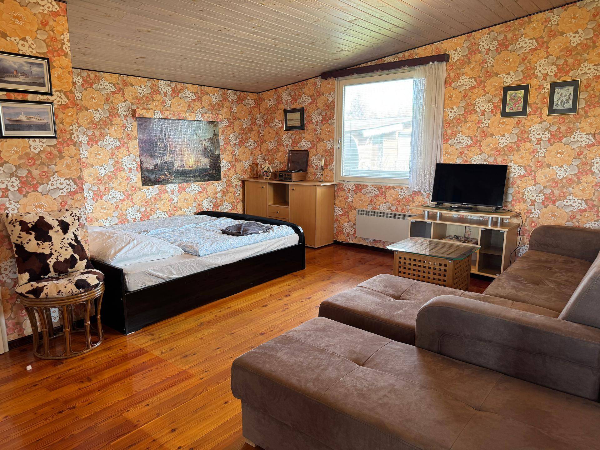 Geräumiger Wohnbereich mit Holzboden, gemusterter Tapete, Sofa und integriertem Schlafbereich.