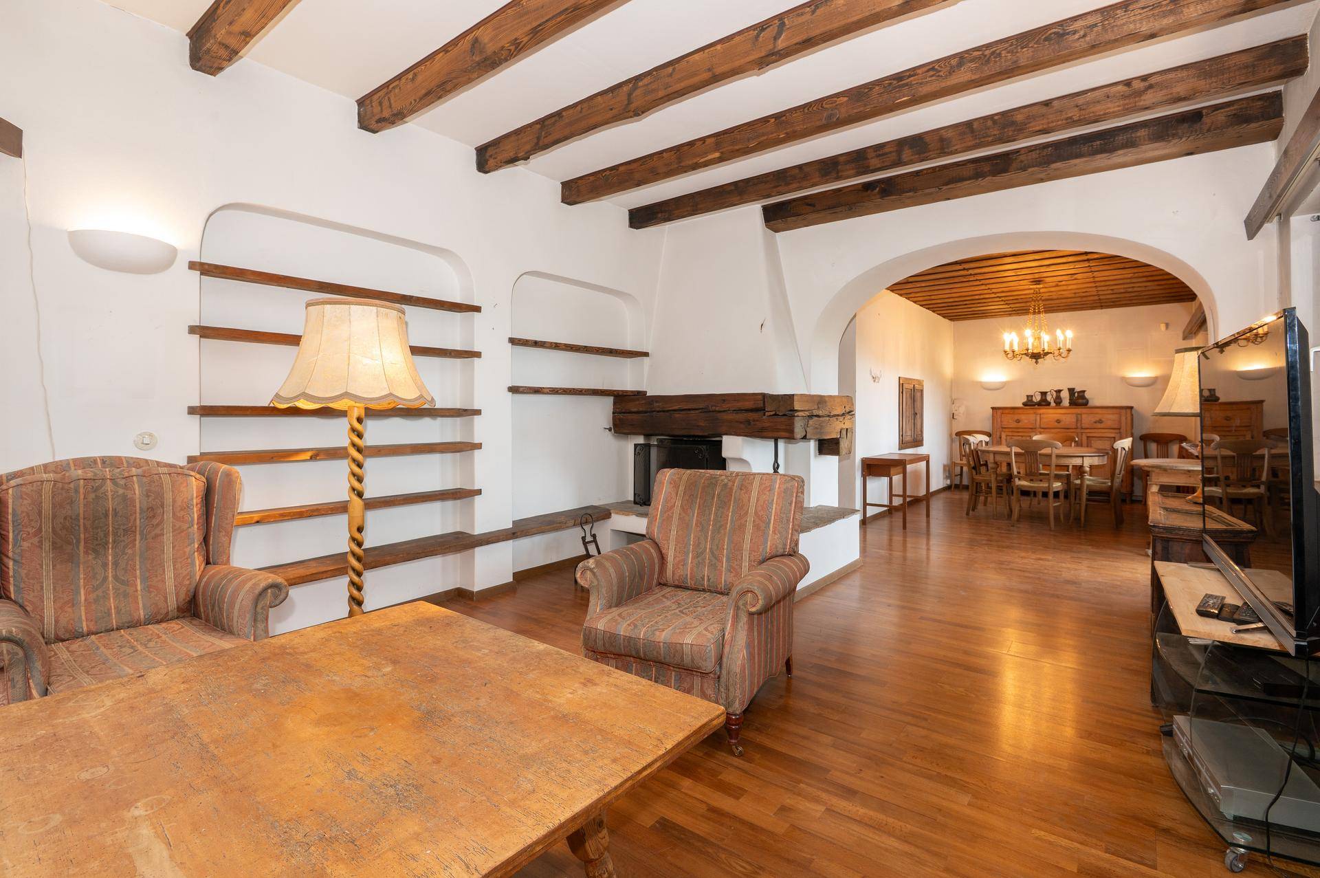 Geräumiges Wohnzimmer mit Holzbalkendecke, Kamin und offenem Zugang zum Essbereich.