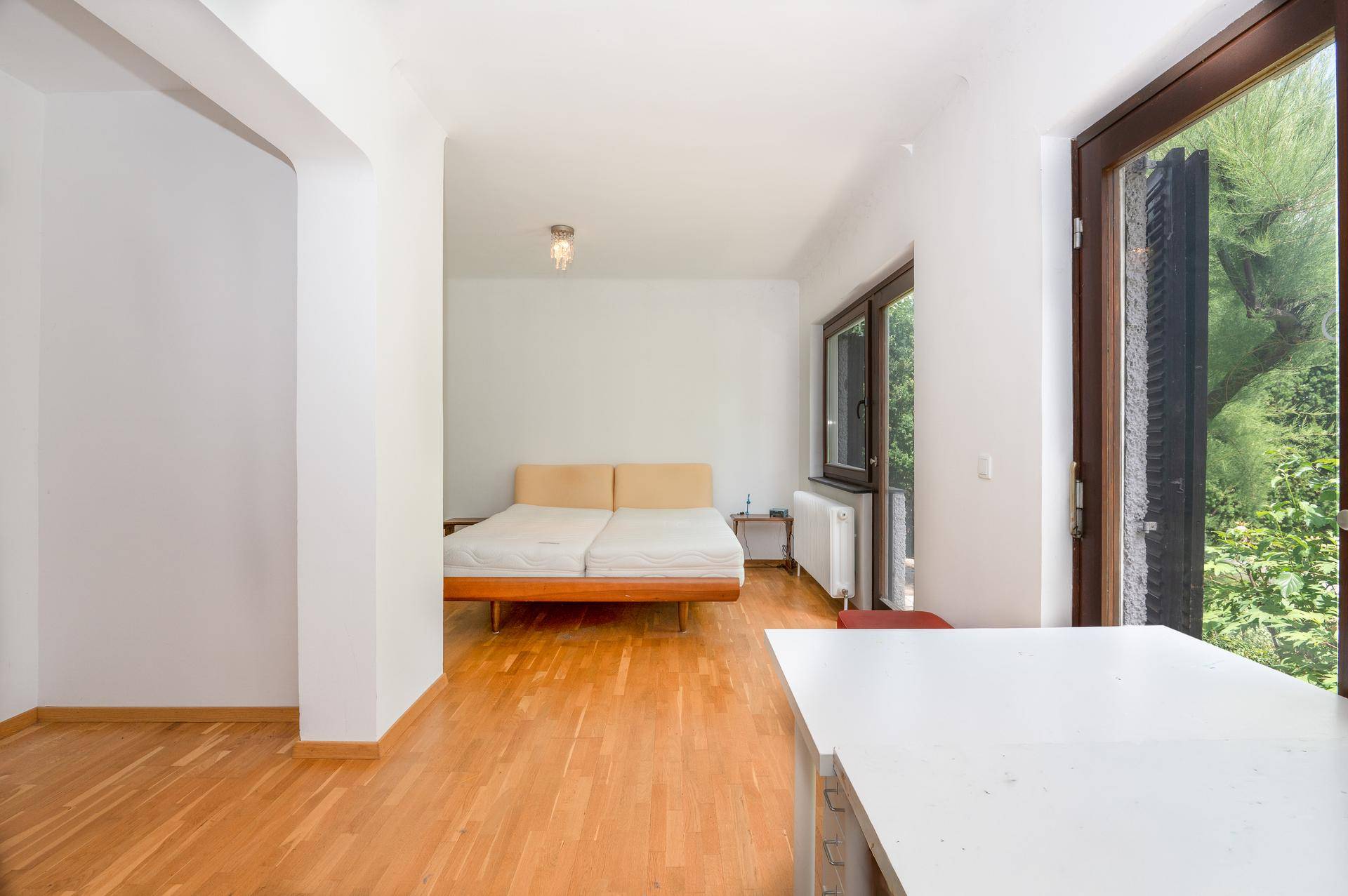 Helles Schlafzimmer mit Holzboden und großen Fenstern, die viel Tageslicht hereinlassen.