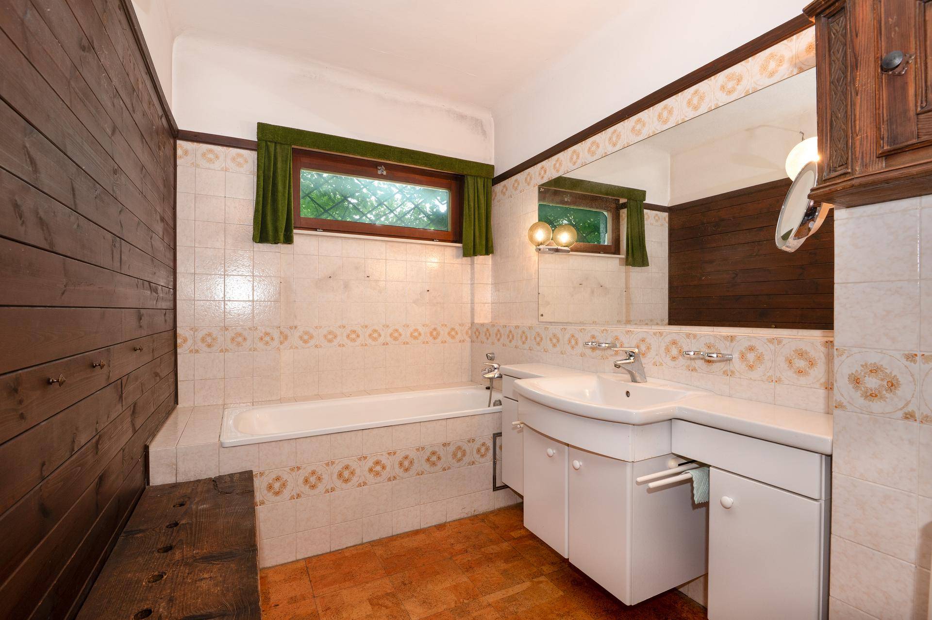 Badezimmer im 80er-Jahre-Stil mit Badewanne, Waschbecken und gemusterten Fliesen.