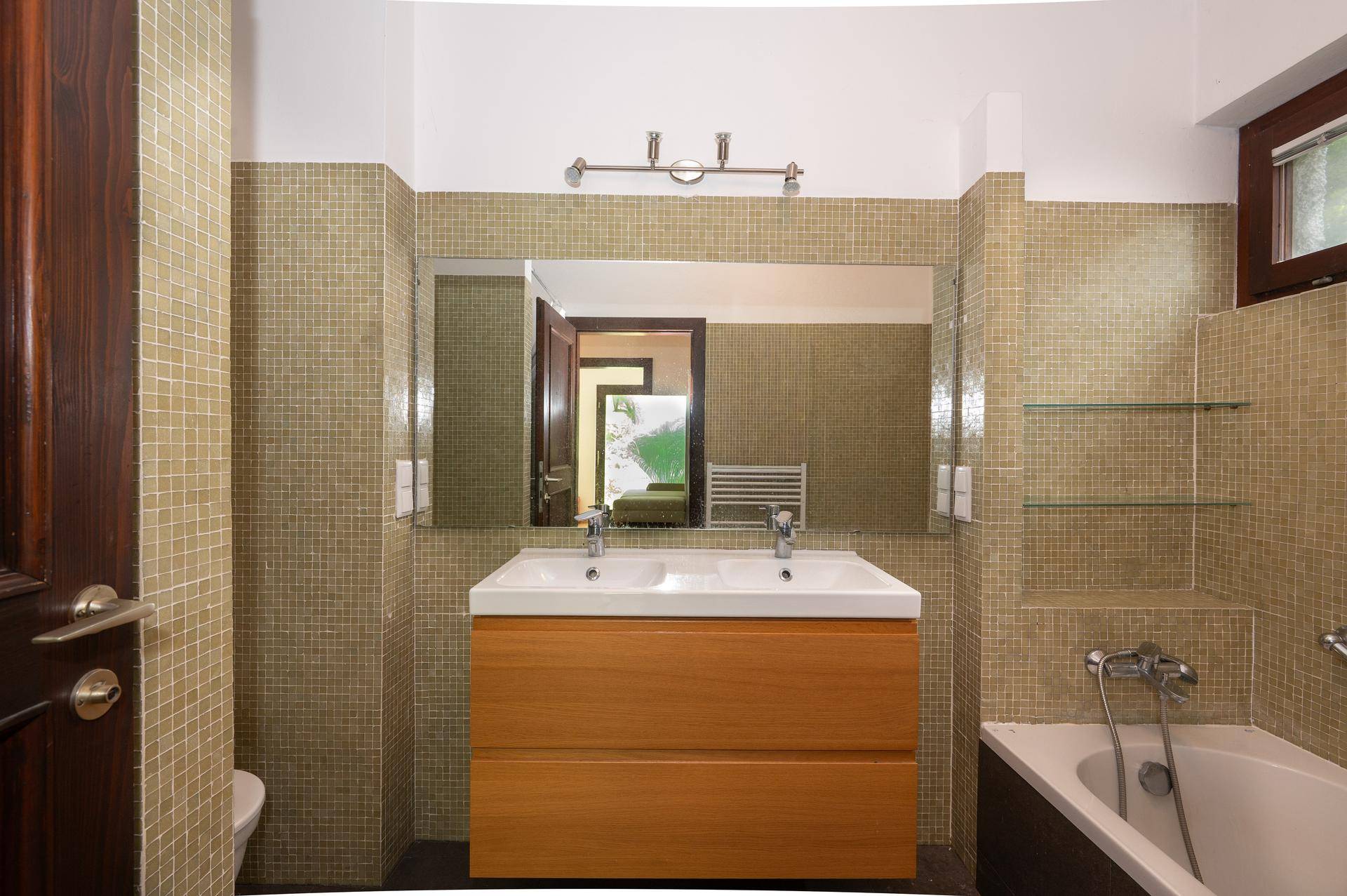 Badezimmer mit Doppelwaschbecken, Mosaikfliesen und Badewanne, gut beleuchtet.
