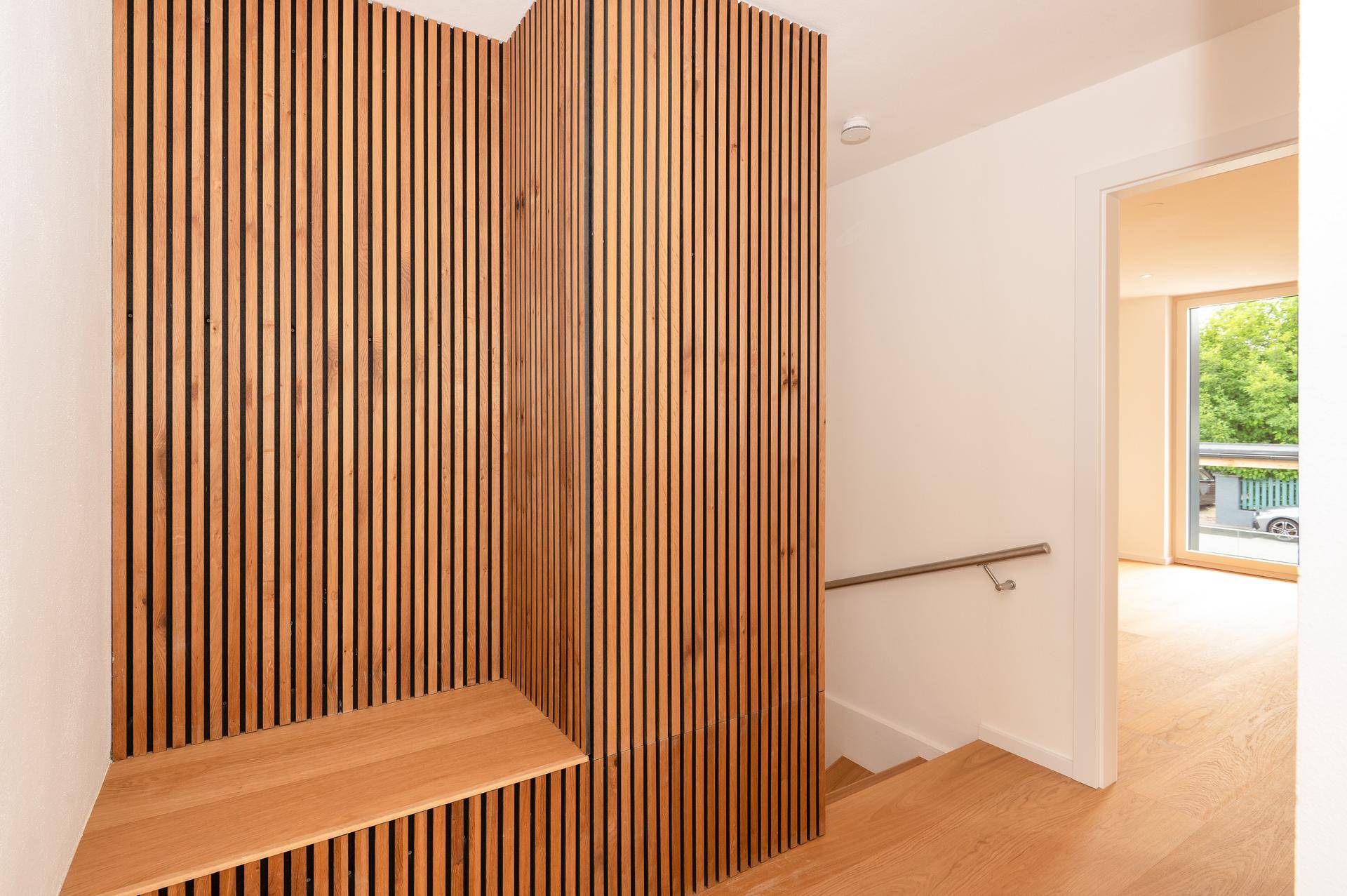 Heller Flur mit Holztreppe, modernem Handlauf und vertikaler Holzverkleidung.