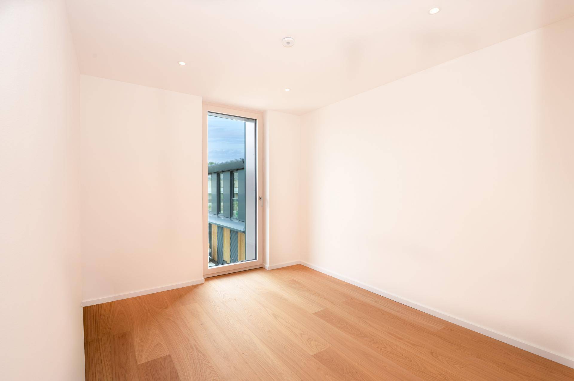 Helles Zimmer mit Parkettboden und großem Fenster, ideal als Schlaf- oder Arbeitszimmer.