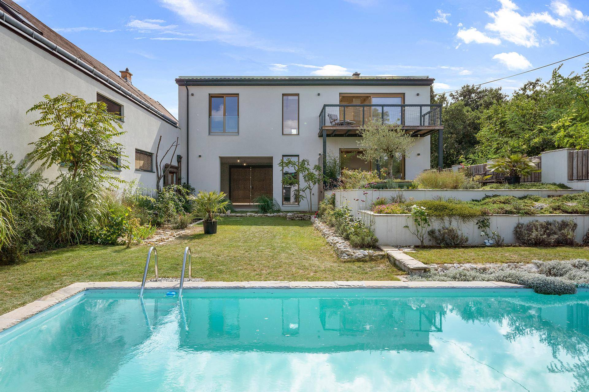 Modernes Haus mit Garten, Pool und Terrassenbereichen unter blauem Himmel.