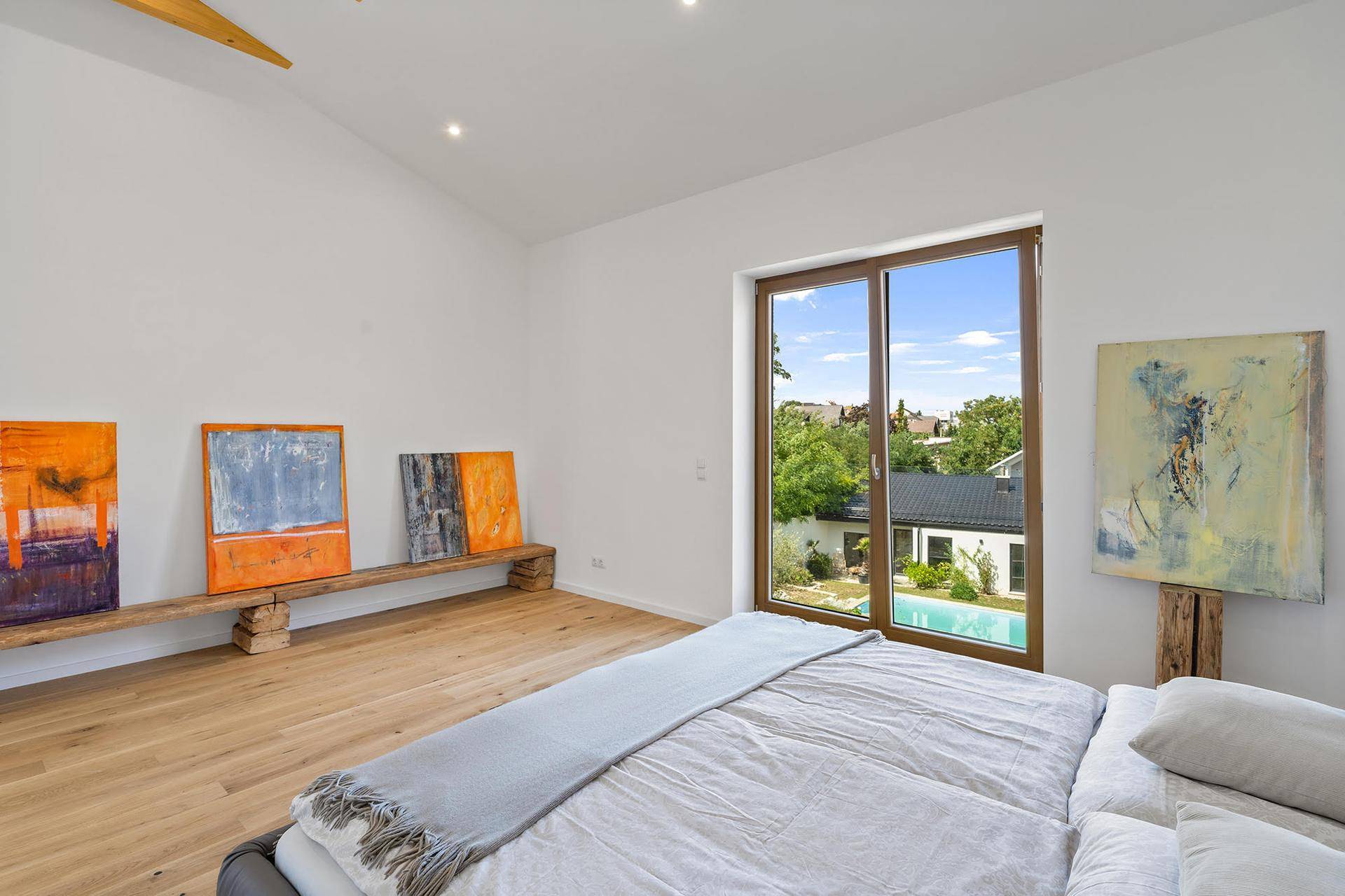 Schlafzimmer mit Holzboden, großen Fenstern und Blick auf den Poolbereich.