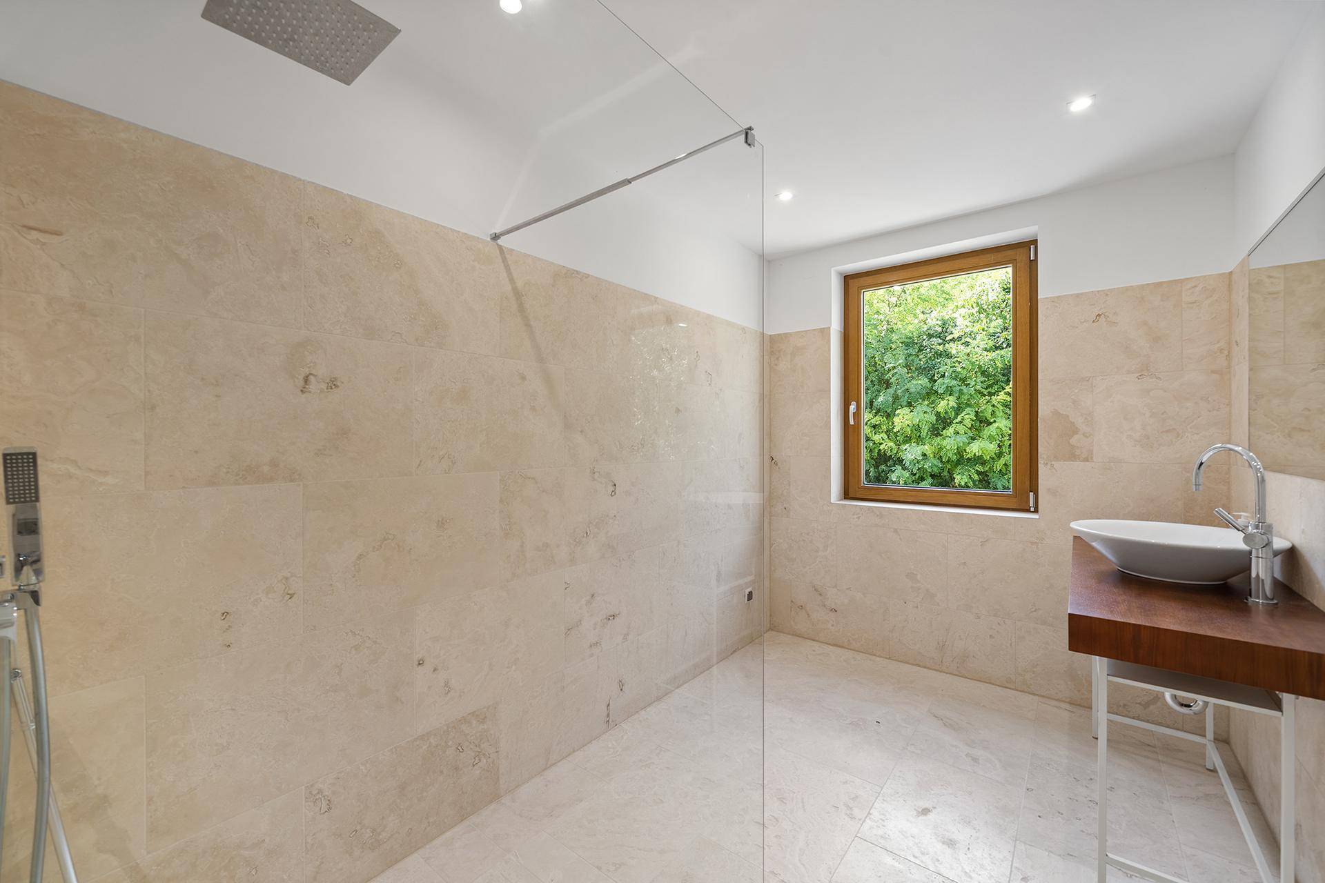 Modernes Badezimmer mit begehbarer Dusche, Fenster und beigefarbenen Fliesen.