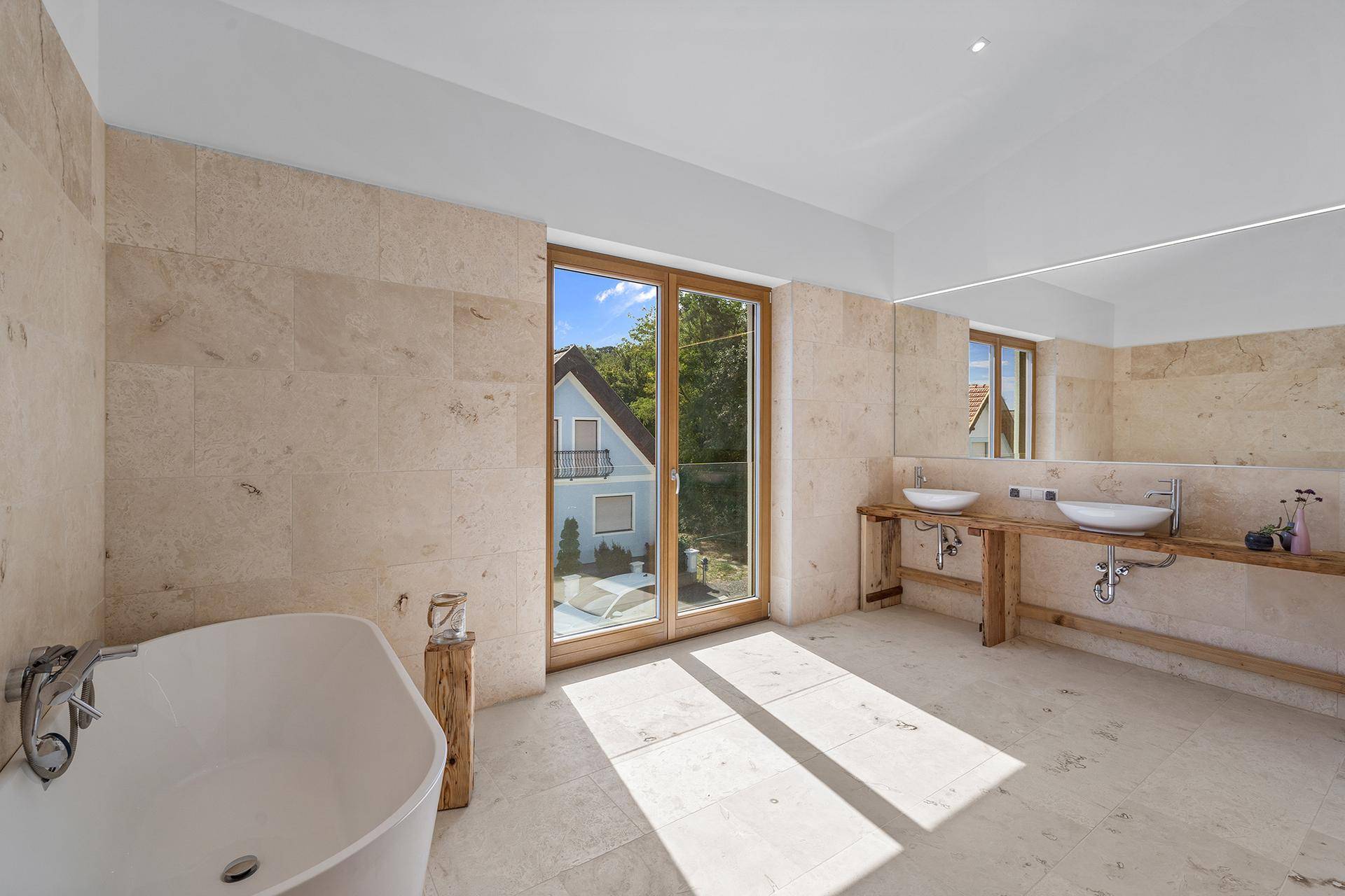 Geräumiges Badezimmer mit freistehender Badewanne, Doppelwaschbecken und großen Fenstern.