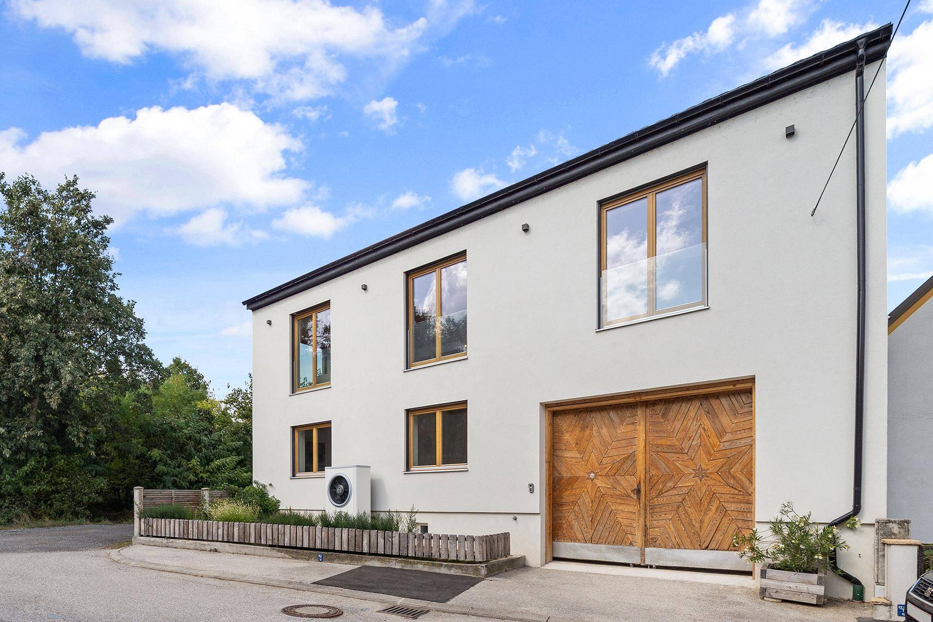 Moderne Hausfassade mit schrägem Dach, Holztor und Wärmepumpe.