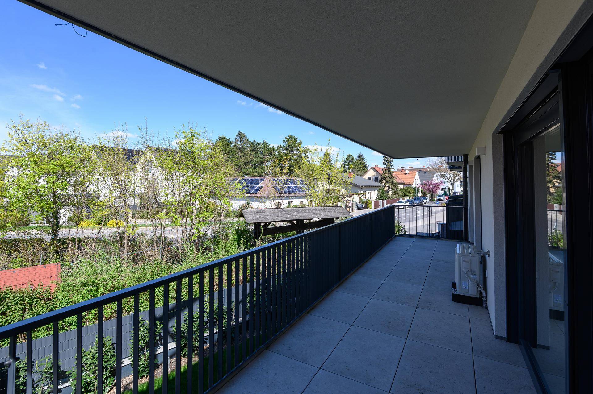 Langer Balkon mit Fliesenboden und weitem Blick über die Nachbarschaft und grüne Umgebung.