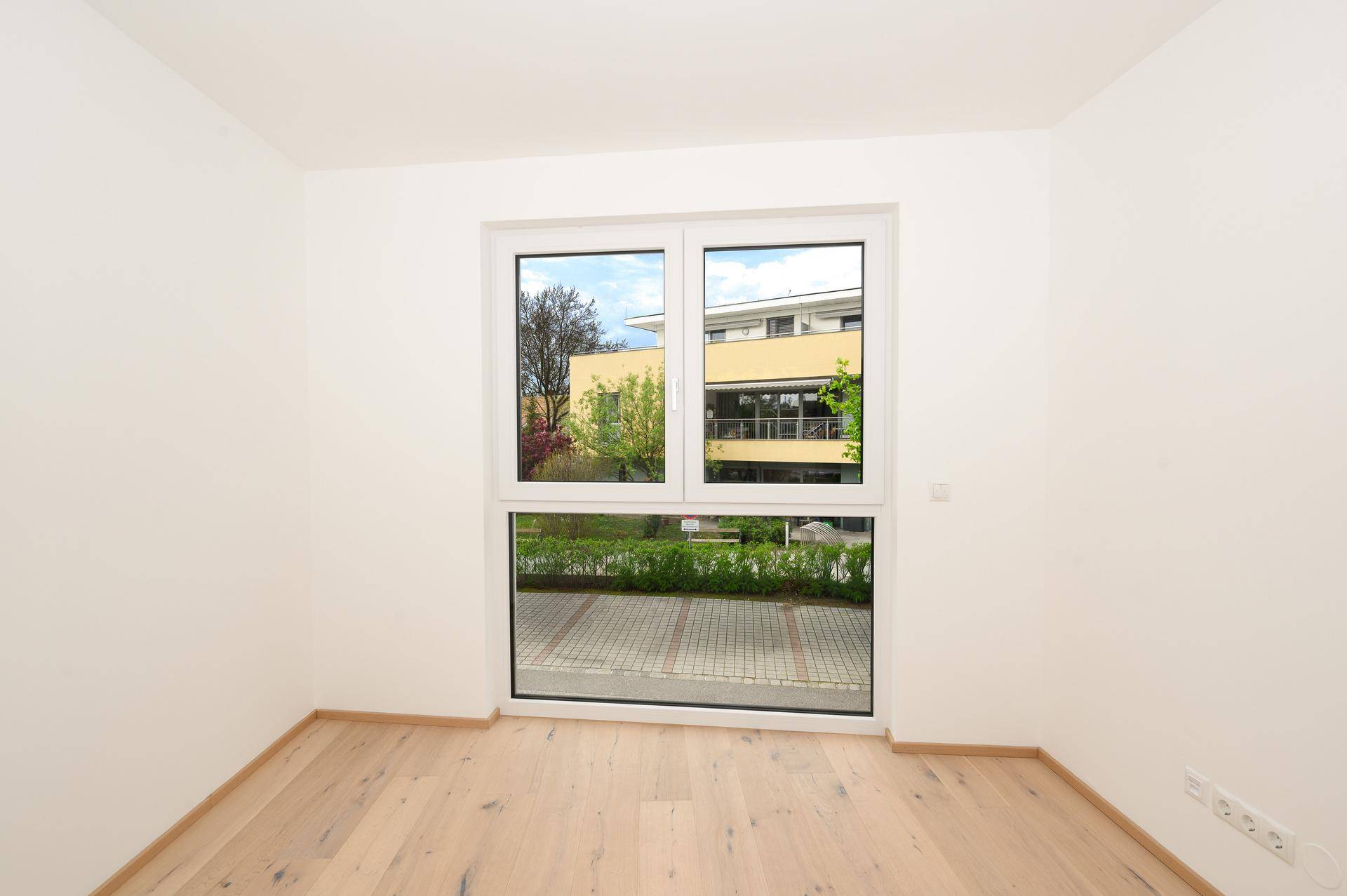 Leerer Raum mit Holzboden und großem Fenster, bietet vielseitige Nutzungsmöglichkeiten.
