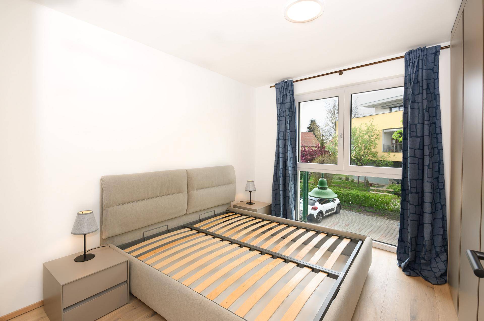 Helles Schlafzimmer mit Holzboden, großem Fenster und Blick ins Grüne.