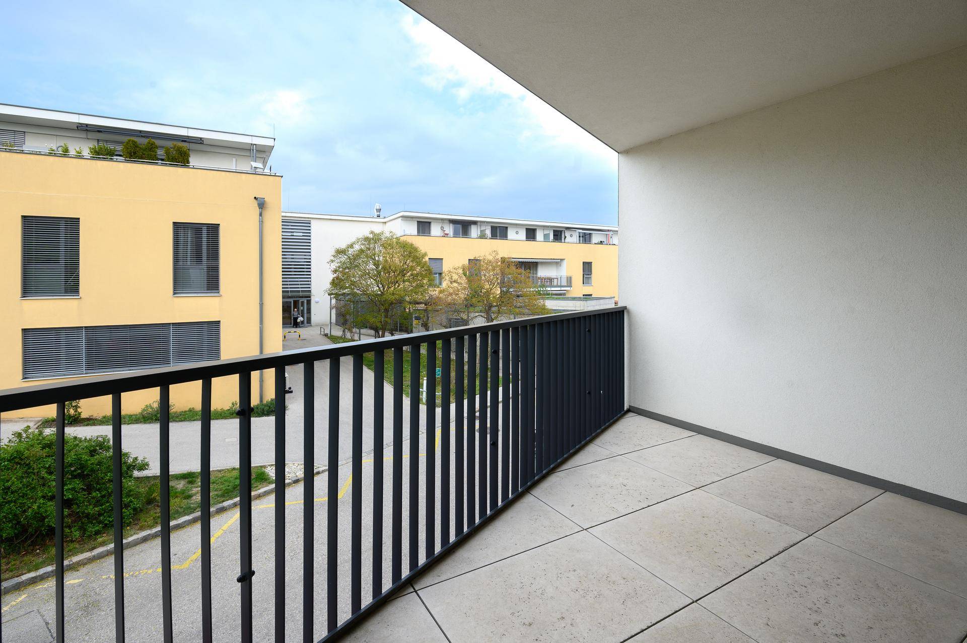 Geräumiger Balkon mit Fliesenboden und Blick auf die umliegenden Gebäude und Grünflächen.