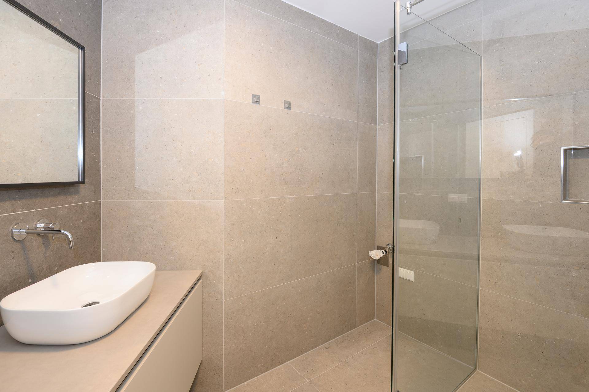 Modernes Badezimmer mit großen Fliesen, begehbarer Dusche und elegantem Waschbecken.