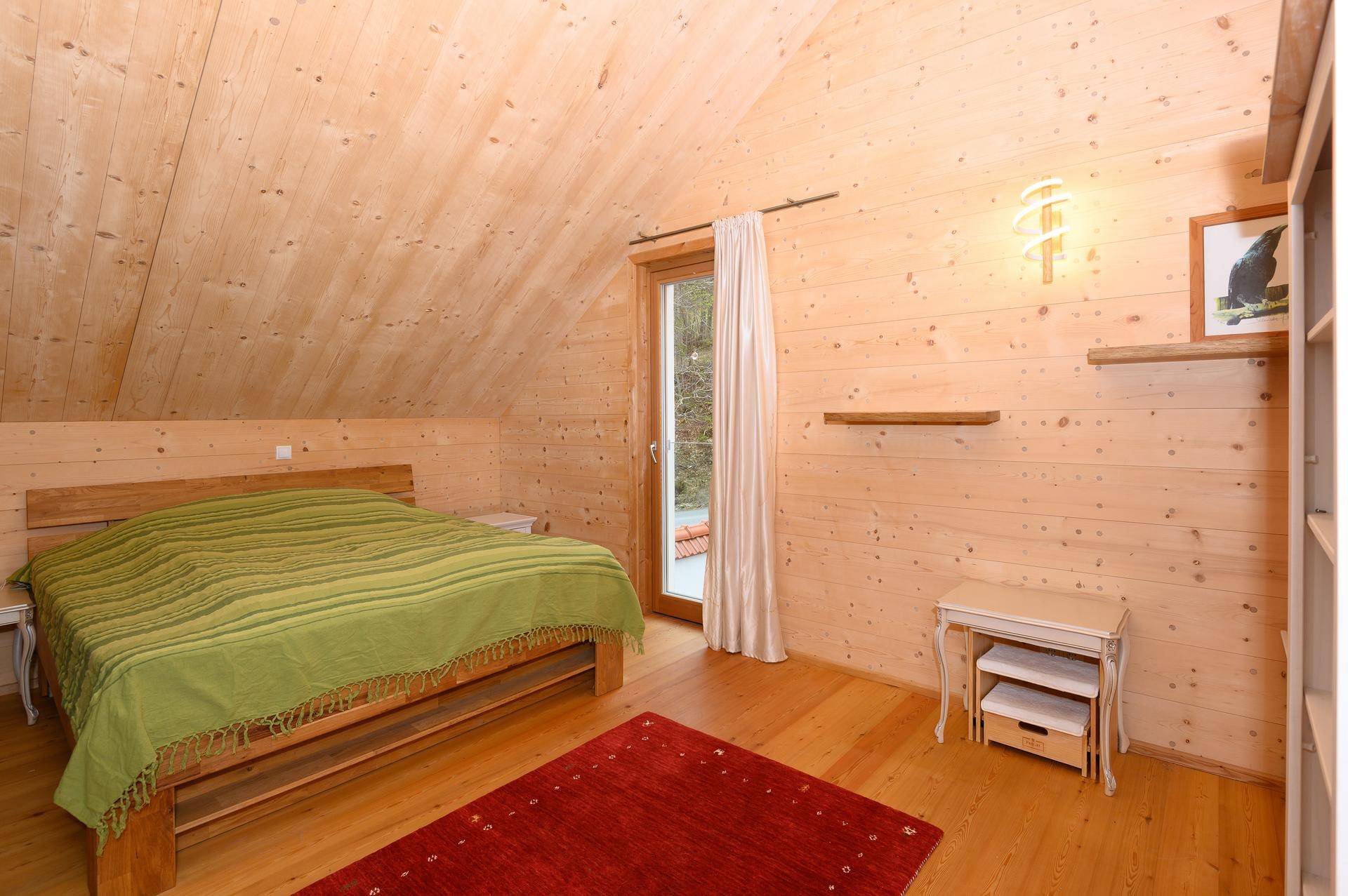 Helles Schlafzimmer mit Holzwänden, Holzboden und Zugang zu einem kleinen Balkon.