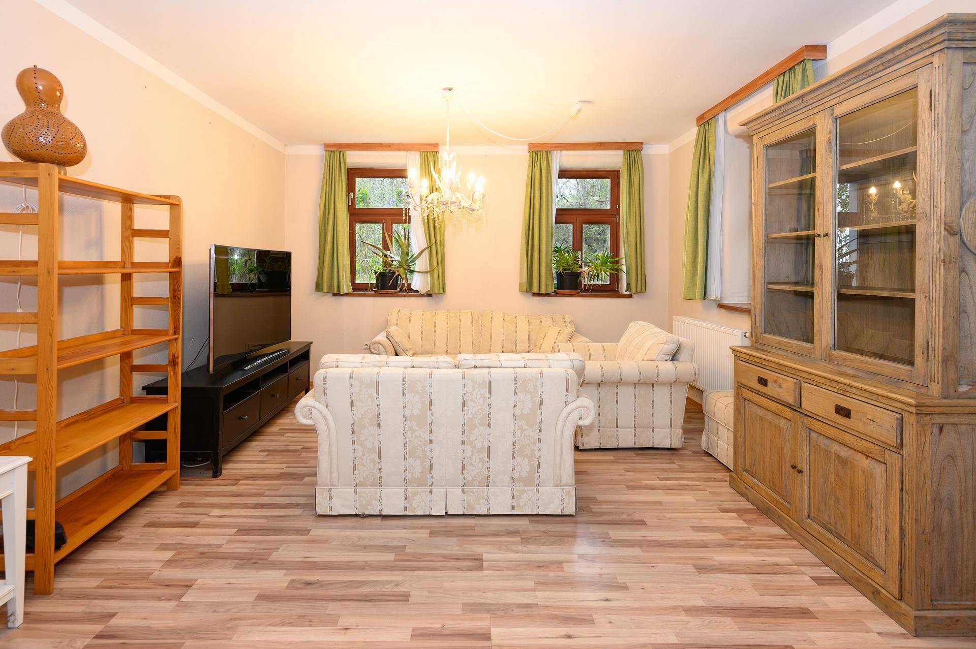 Geräumiges Wohnzimmer mit Laminatboden, traditionellen Möbeln und grünen Vorhängen.