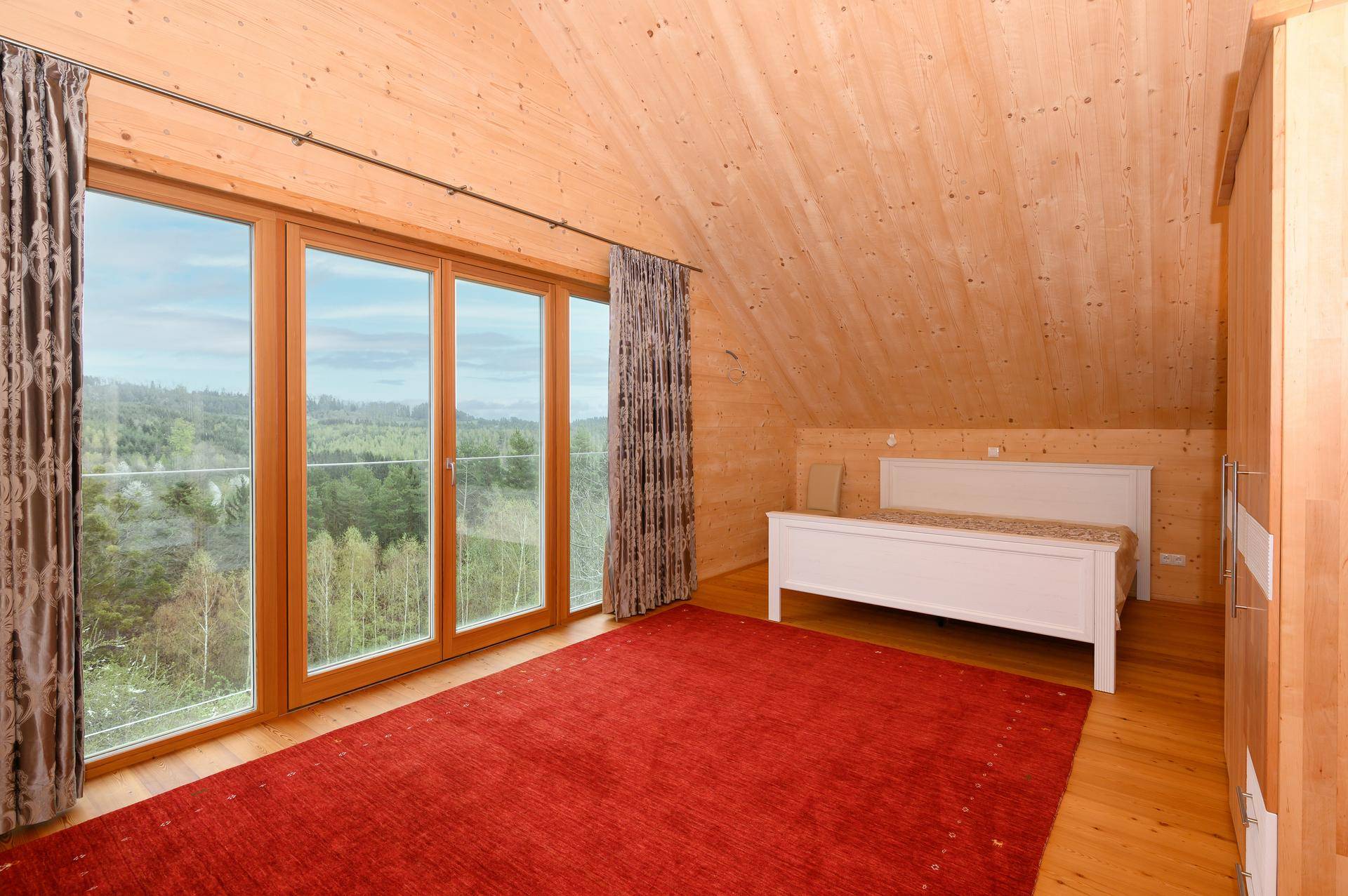 Schlafzimmer mit Holzwänden, Holzboden und großen Fenstern mit Waldblick.