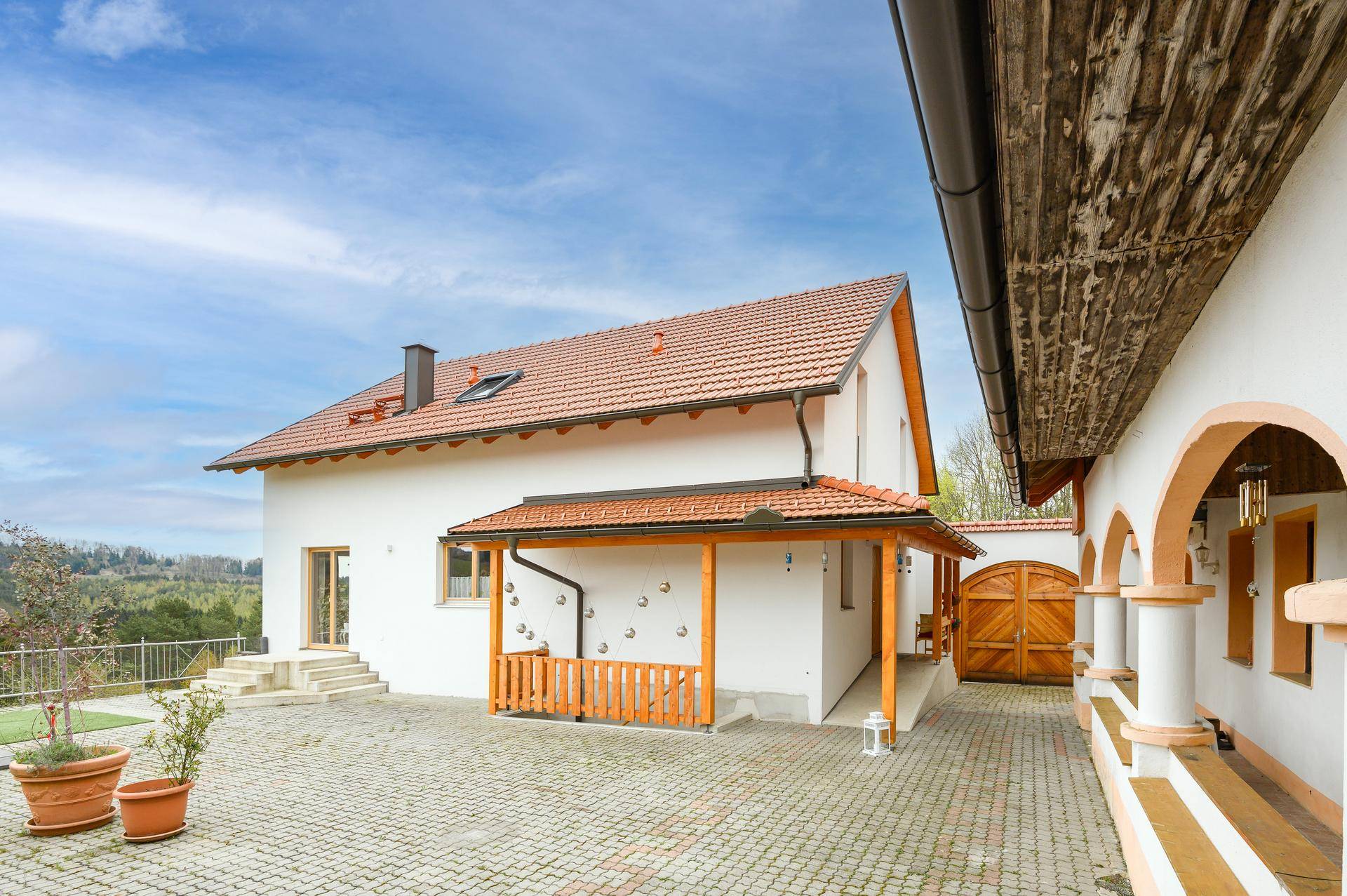 Innenhof mit gepflastertem Bereich, Holzveranda und Blick auf die umliegende Natur.