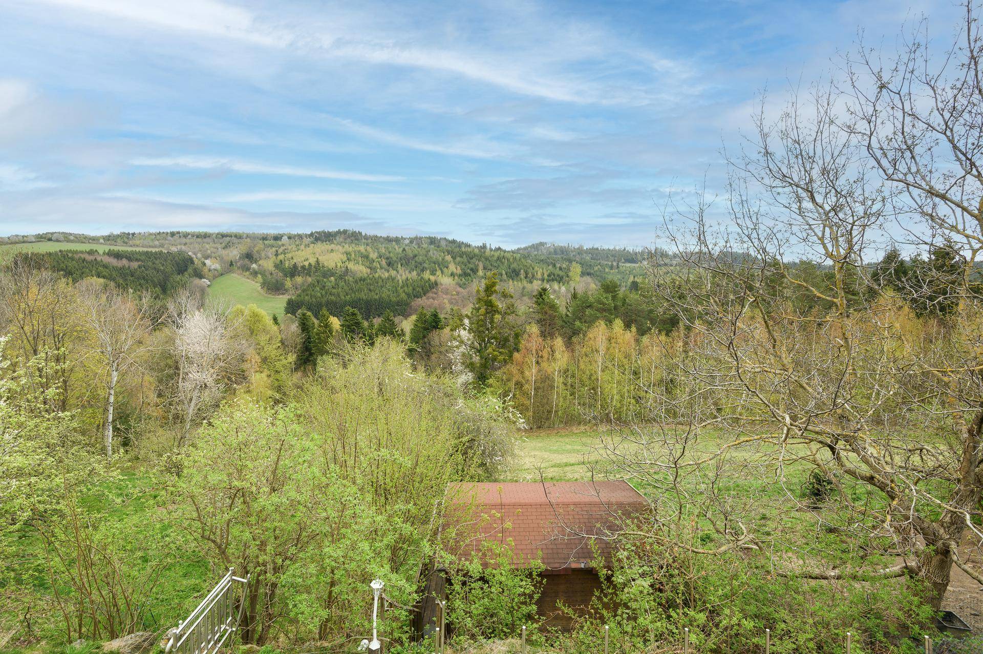 Malerischer Ausblick über die hügelige, grüne Landschaft mit Wäldern und Wiesen.