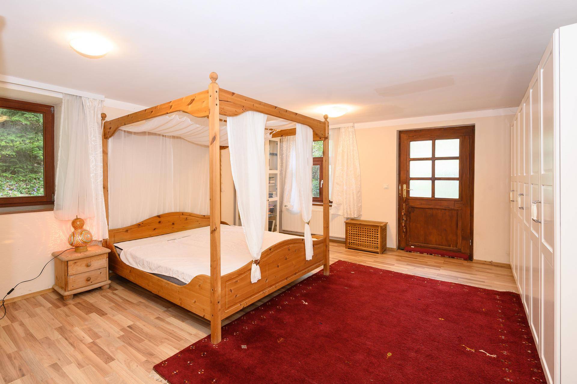 Schlafzimmer mit Himmelbett, Laminatboden und großem weißen Kleiderschrank.