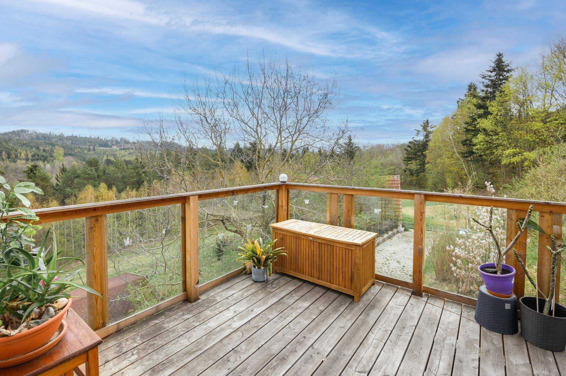 Großer Holzbalkon mit Glasgeländer und weitem Blick über die grüne Landschaft.