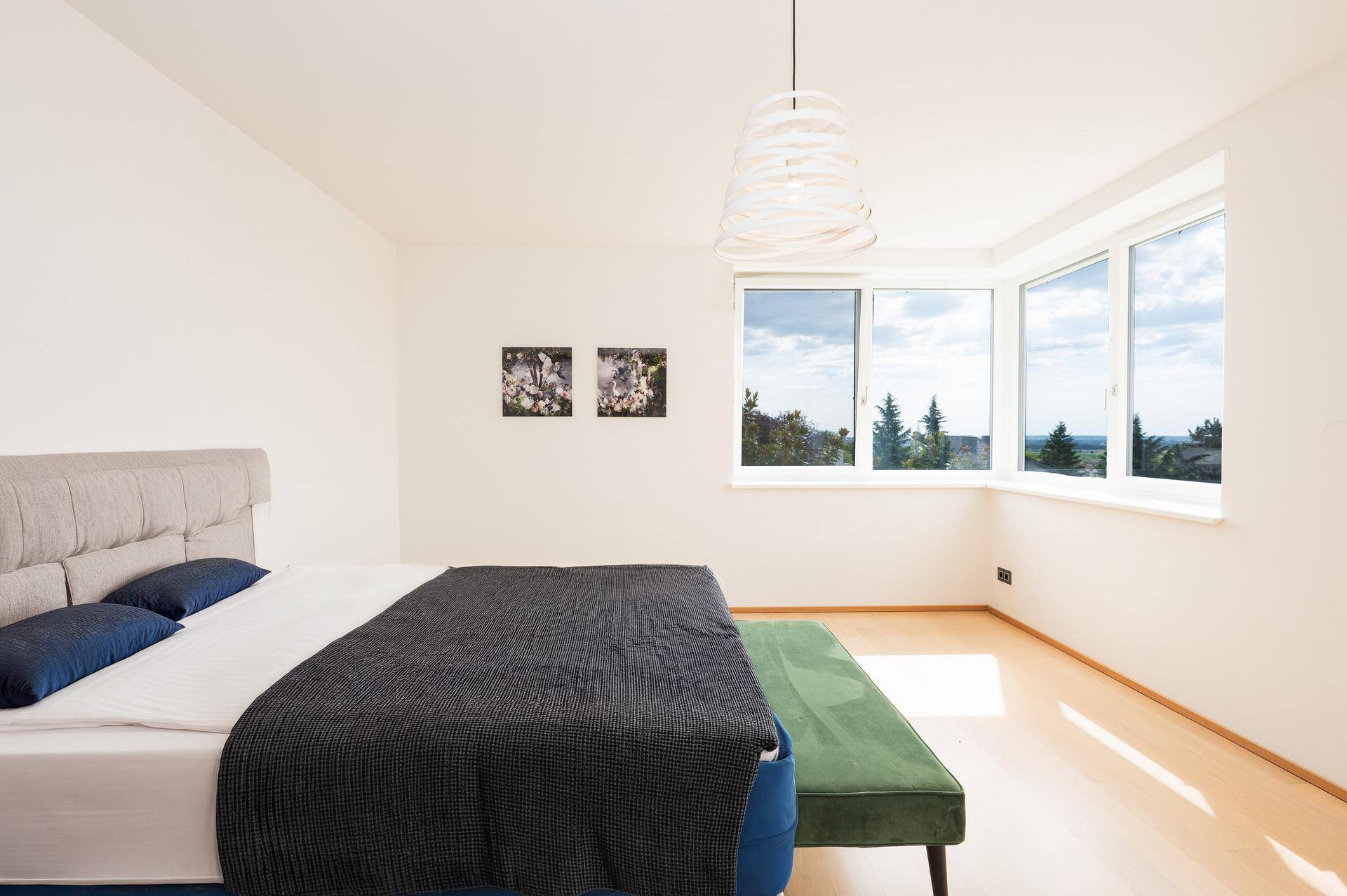 Geräumiges Schlafzimmer mit großem Bett, Holzboden und Erkerfenstern mit schöner Aussicht.
