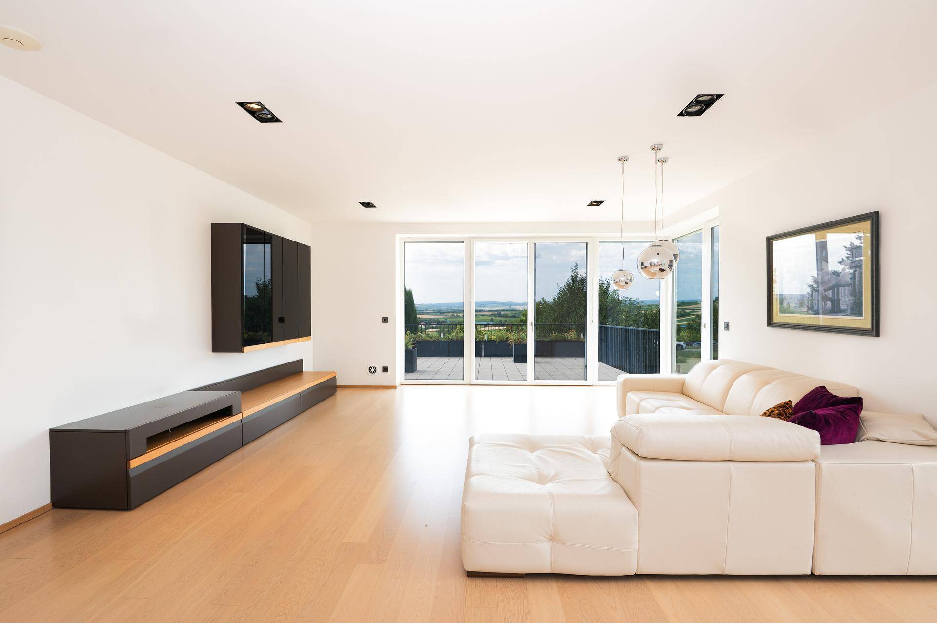 Helles Wohnzimmer mit modernem Sofa, Holzboden und großen Fenstern mit weitem Ausblick.
