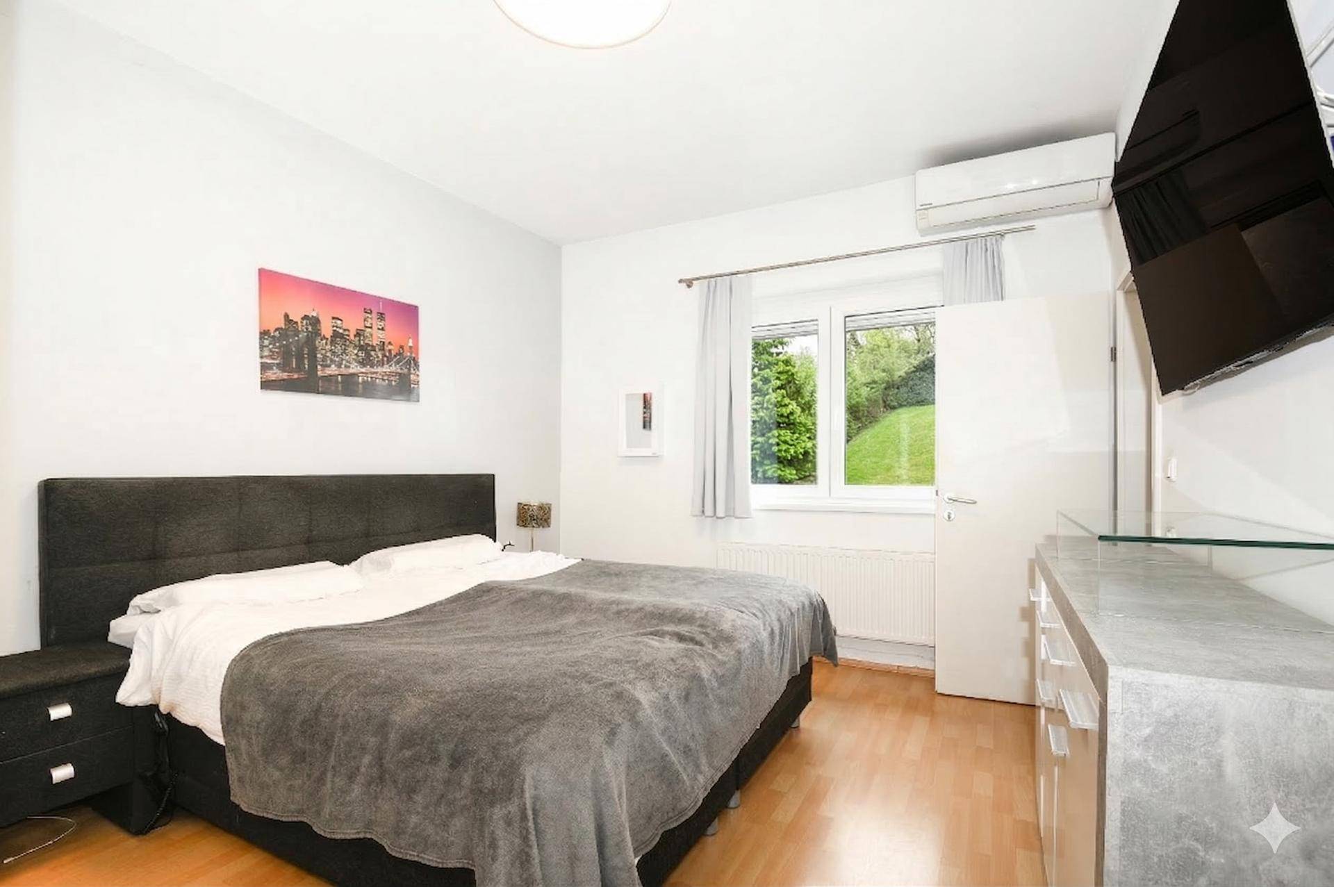 Schlafzimmer mit Doppelbett, Holzboden, Klimaanlage und Blick in den Garten.