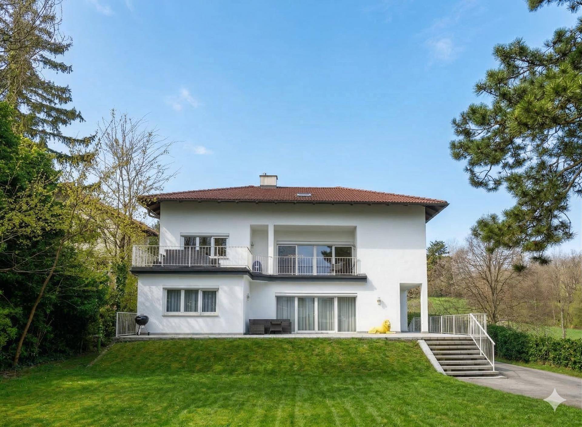 Freistehendes weißes Haus mit Balkonen, Terrasse und großem Garten auf einem Hügel.