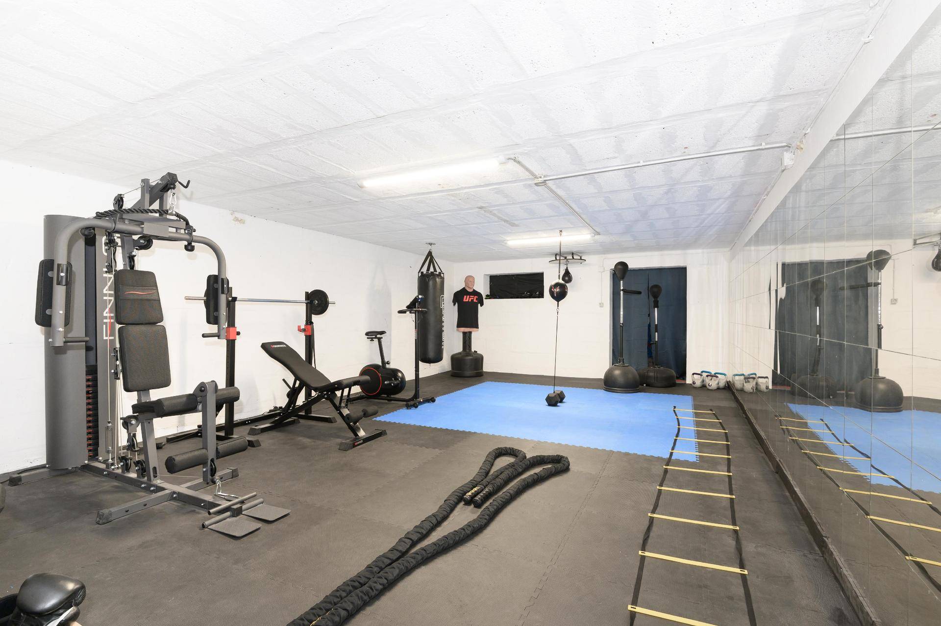 Geräumiger Fitnessraum mit verschiedenen Trainingsgeräten, Spiegelwand und Gummiboden.