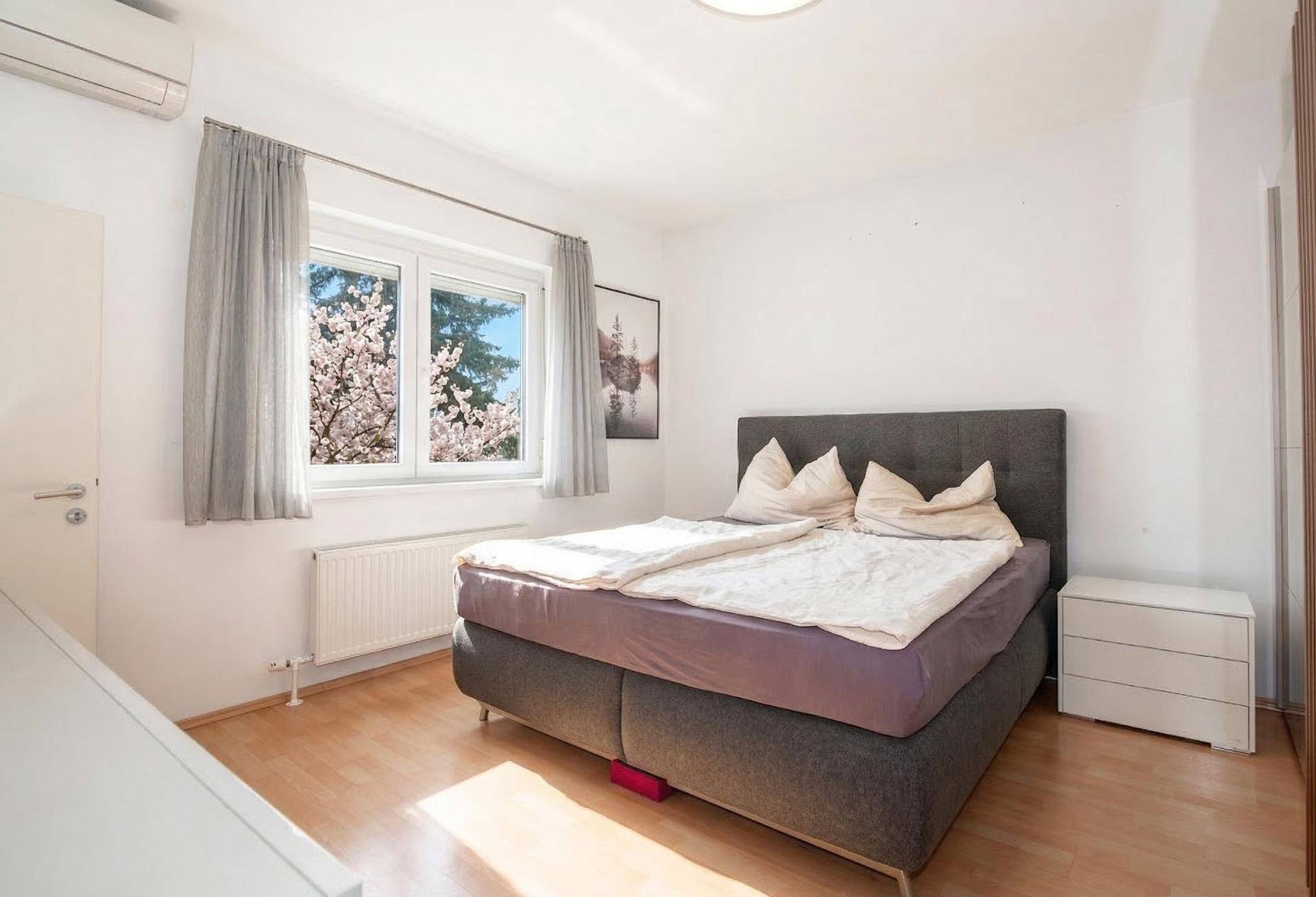 Helles Schlafzimmer mit Doppelbett, Holzboden, Klimaanlage und Blick ins Grüne.