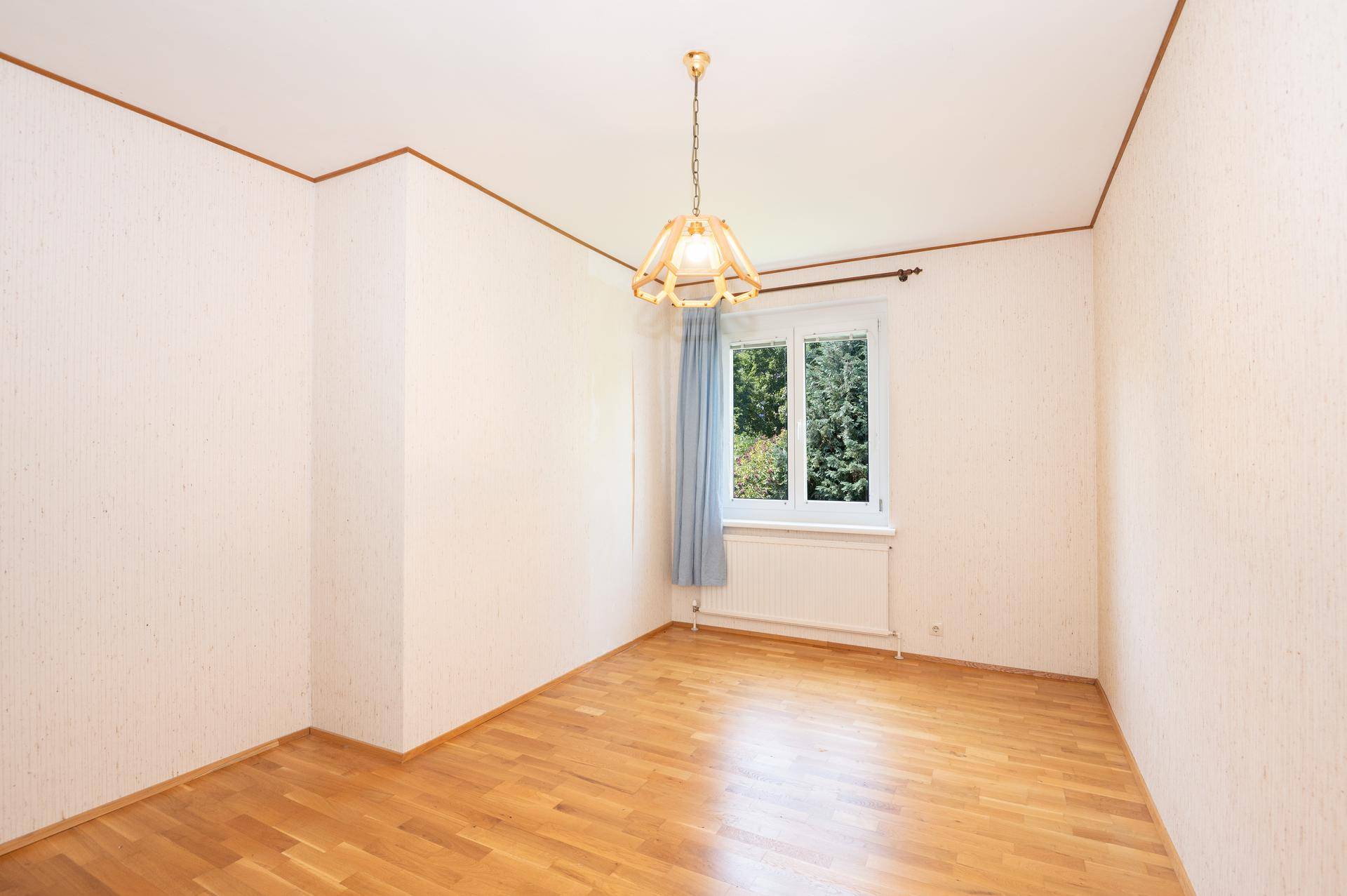 Geräumiges Zimmer mit Parkettboden und Fenster, das viel Tageslicht hereinlässt.