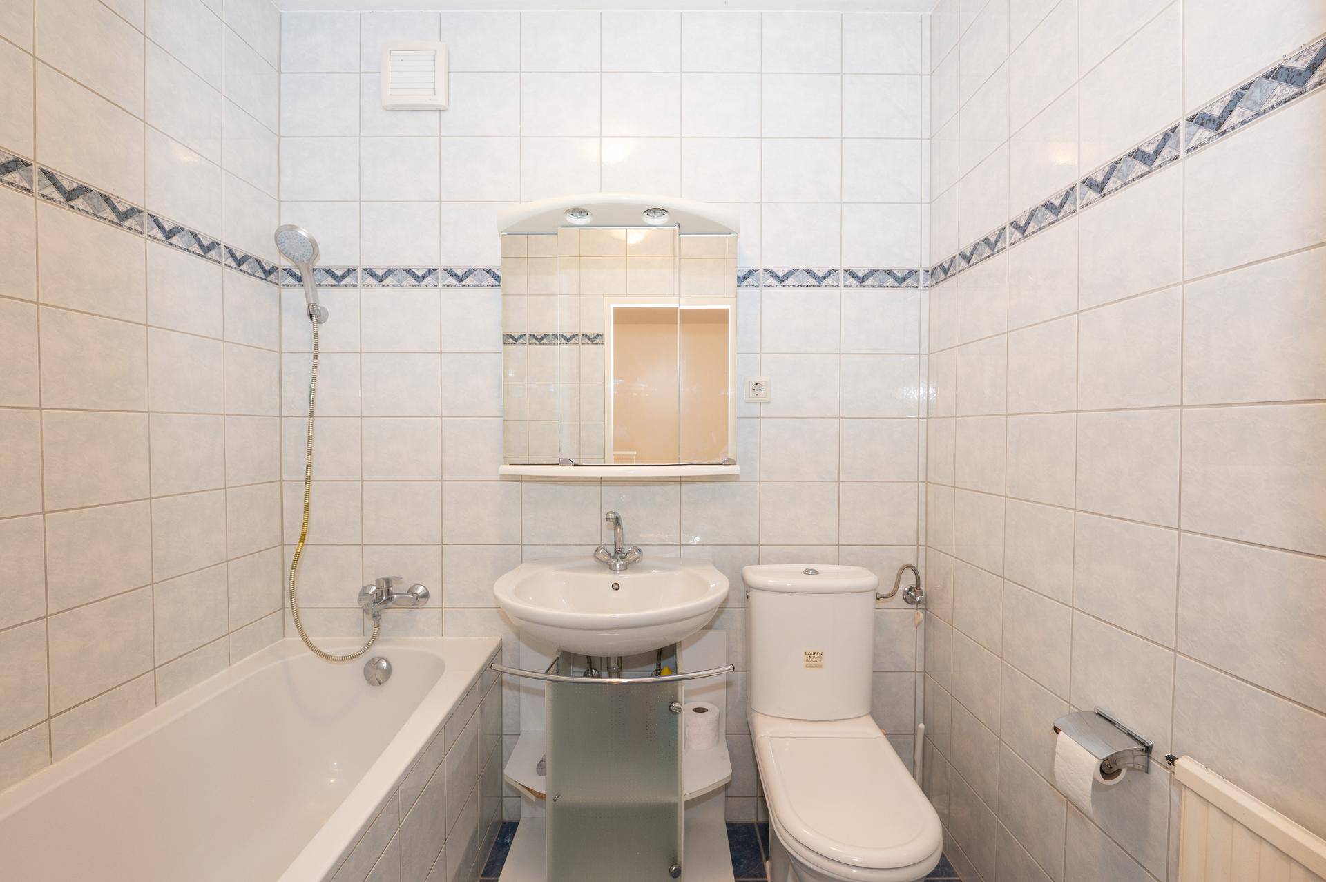 Gefliestes Badezimmer mit Badewanne, WC, Waschbecken und Spiegelschrank in hellem Design.