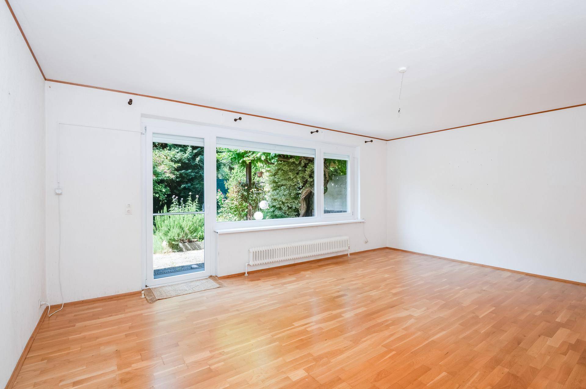 Heller Wohnraum mit Parkettboden und großem Fenster mit direktem Zugang zum Garten.