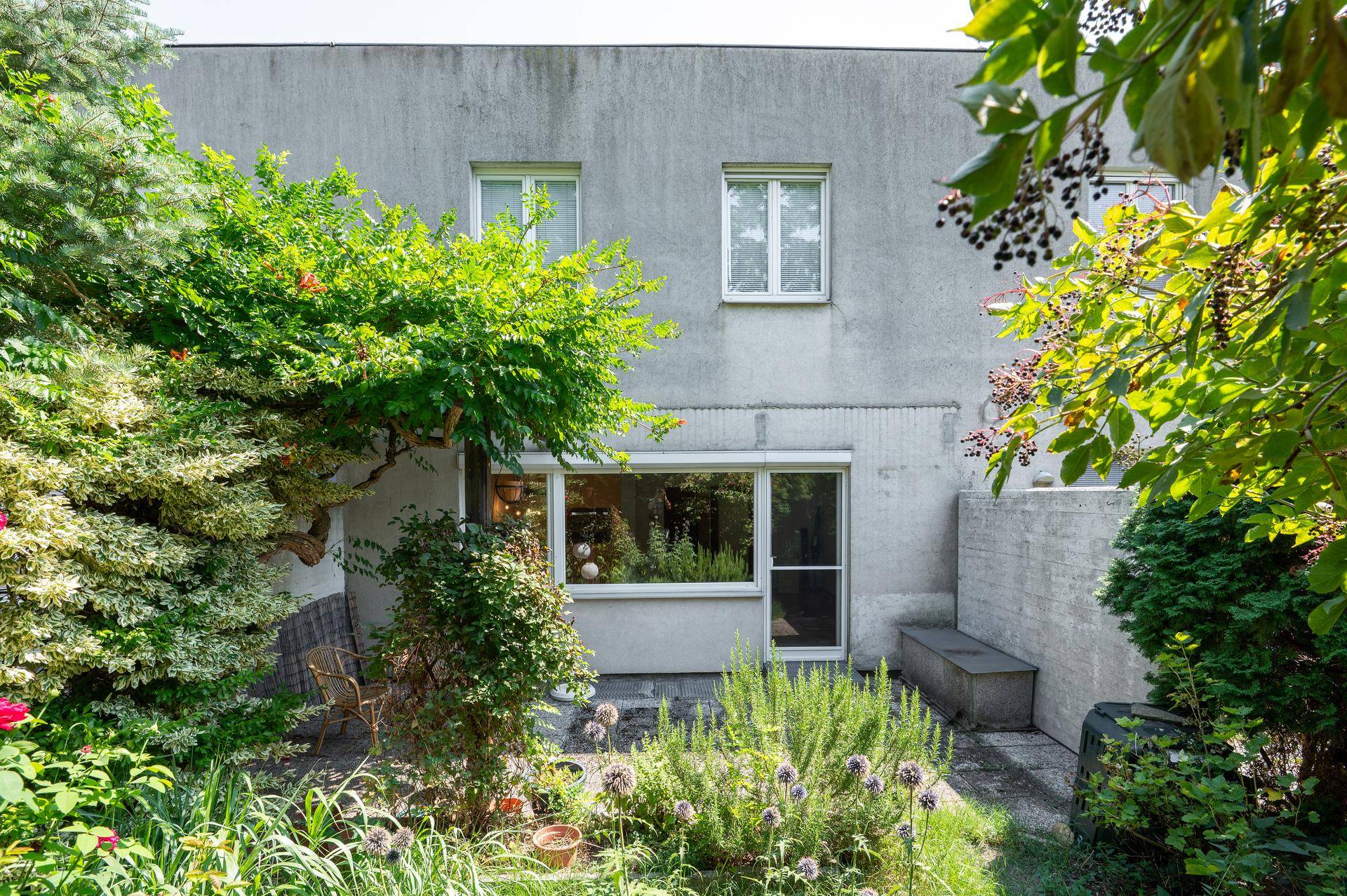 Rückseite des Hauses mit kleiner Terrasse und gepflegtem Gartenbereich unter blauem Himmel.