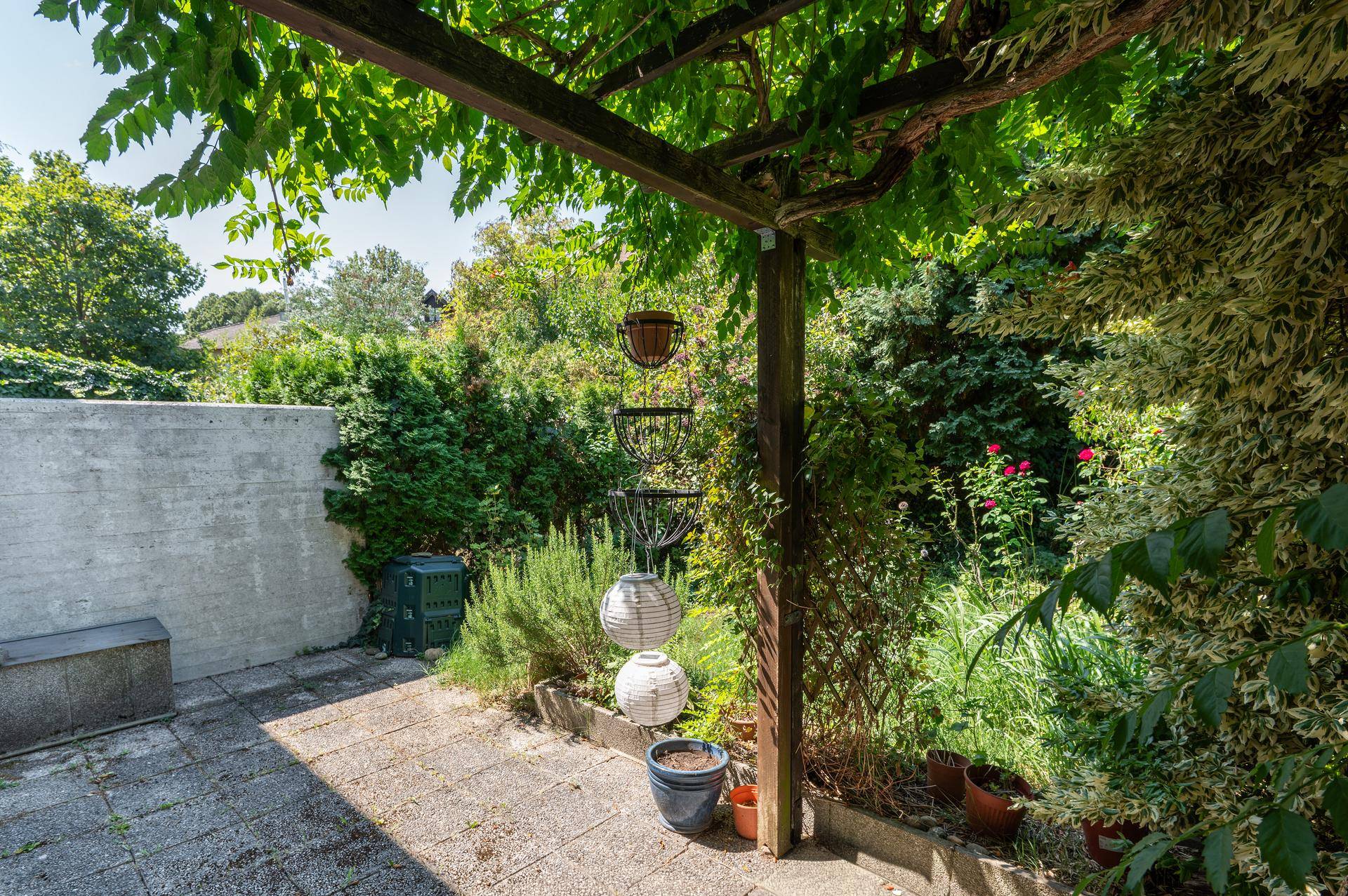 Sonniger Terrassenbereich mit Pergola und üppiger Vegetation, ideal für entspannte Stunden im Freien.