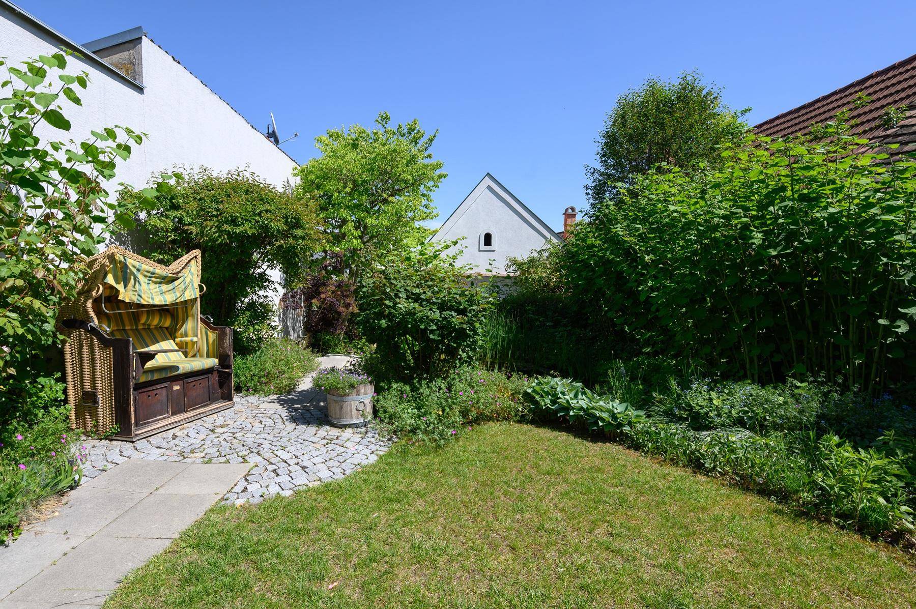 Kleiner, gepflegter Gartenbereich mit Strandkorb und grüner Bepflanzung.