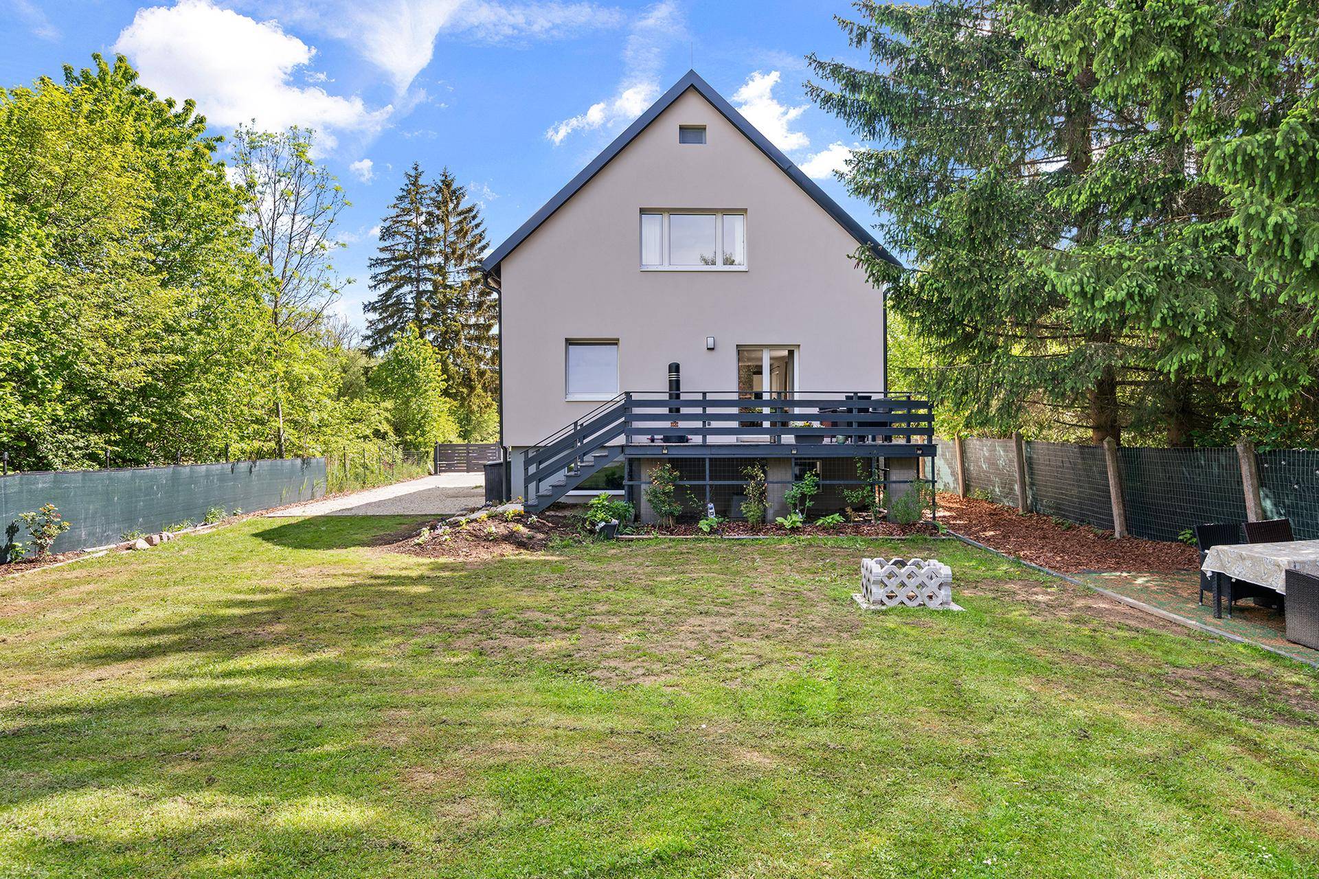 Rückseite des Hauses mit großer Holzterrasse, weitläufiger Rasenfläche und viel Grün.